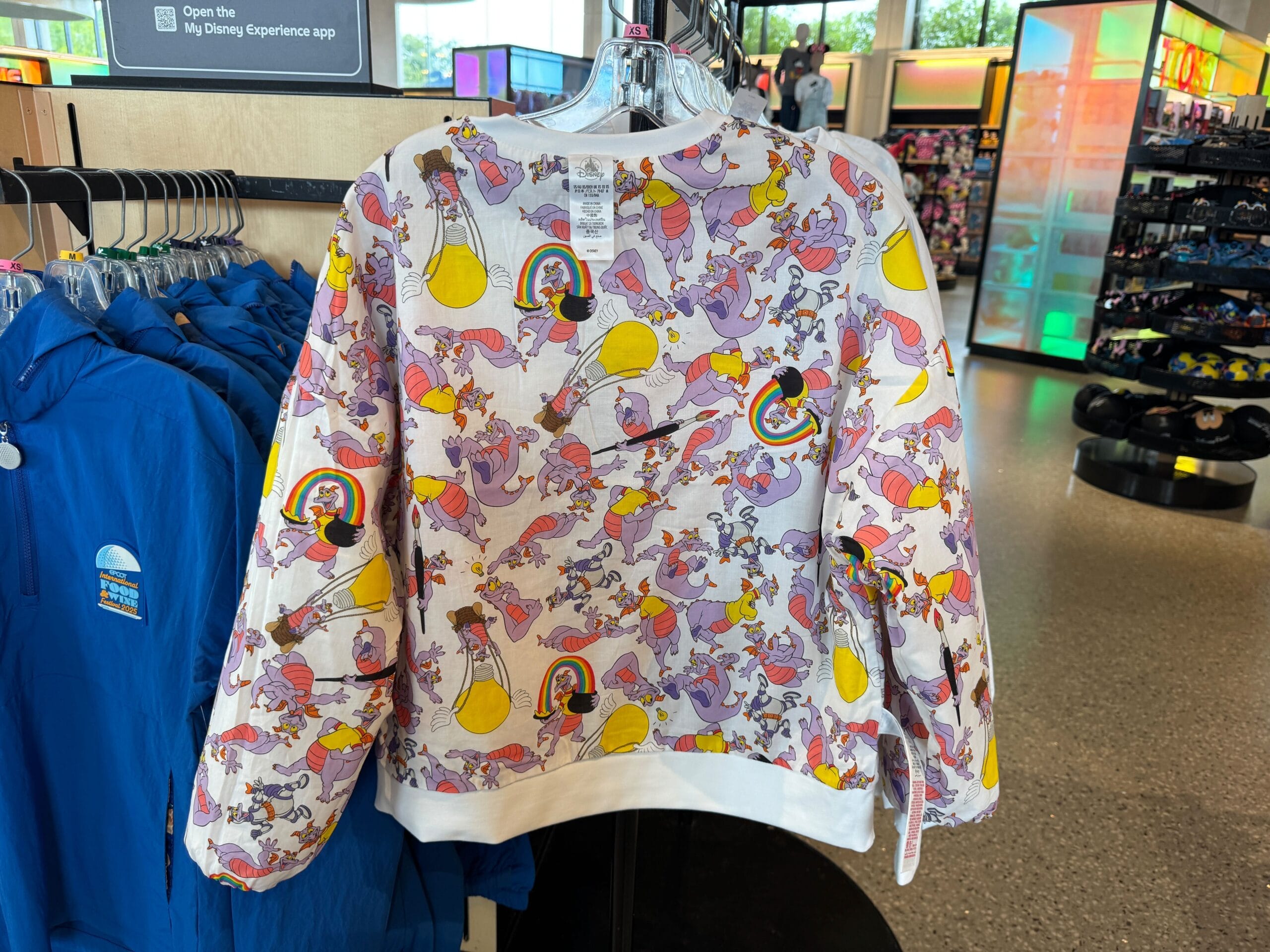 A colorful sweatshirt featuring an all-over Dumbo pattern hangs on a rack in a retail store.