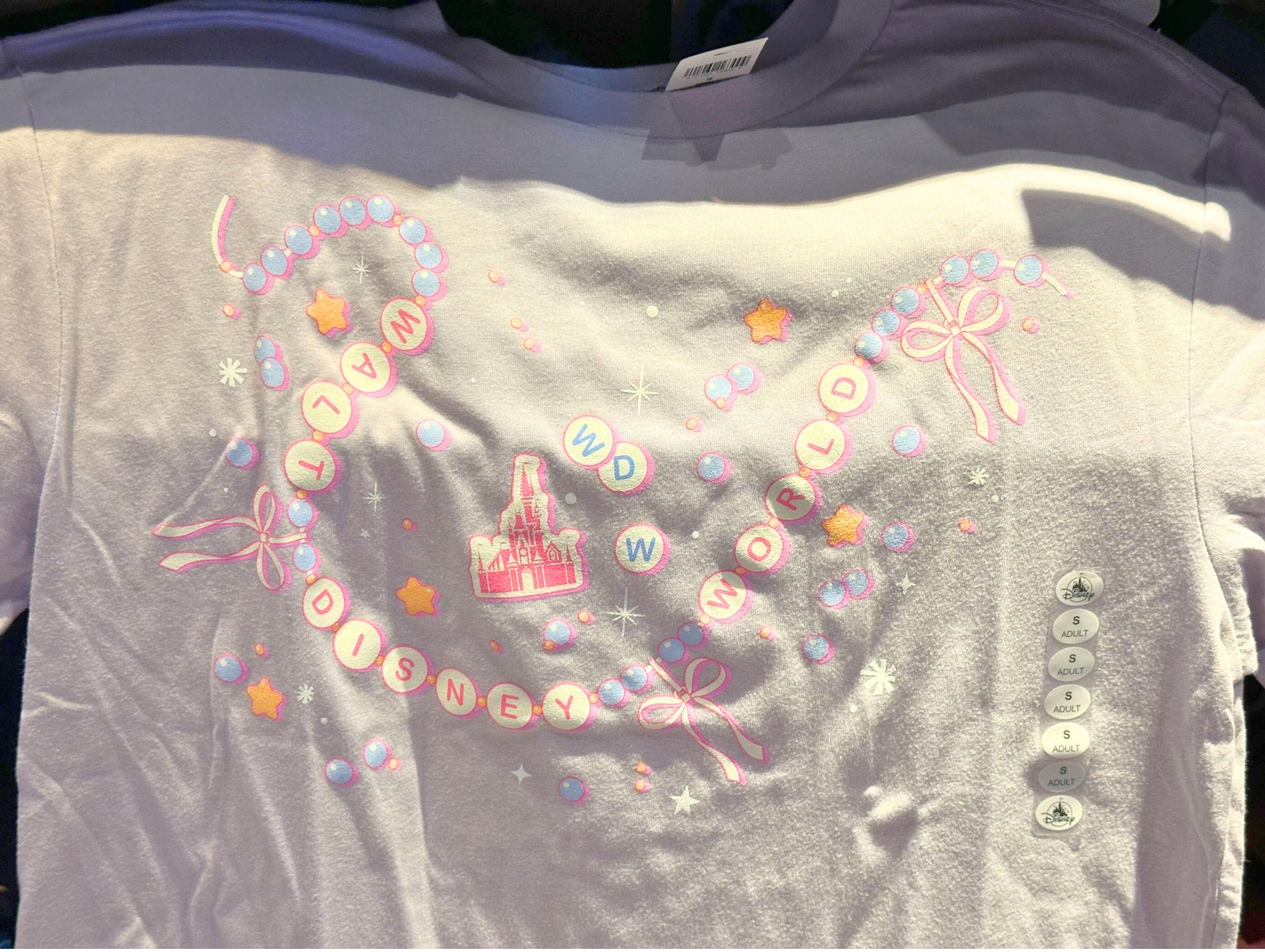 White shirt with "Walt Disney World" in pink letters, beads, stars, and a pink castle graphic in the center.