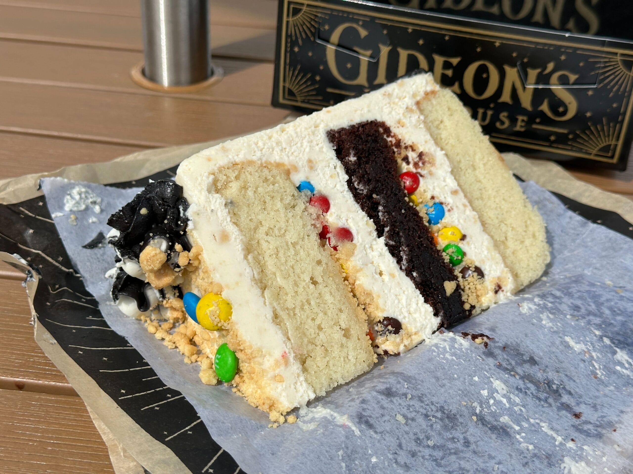 A slice of Bride of Frankenstein Cake topped with M&M candies and white frosting on parchment, a treat reminiscent of Disney parks.
