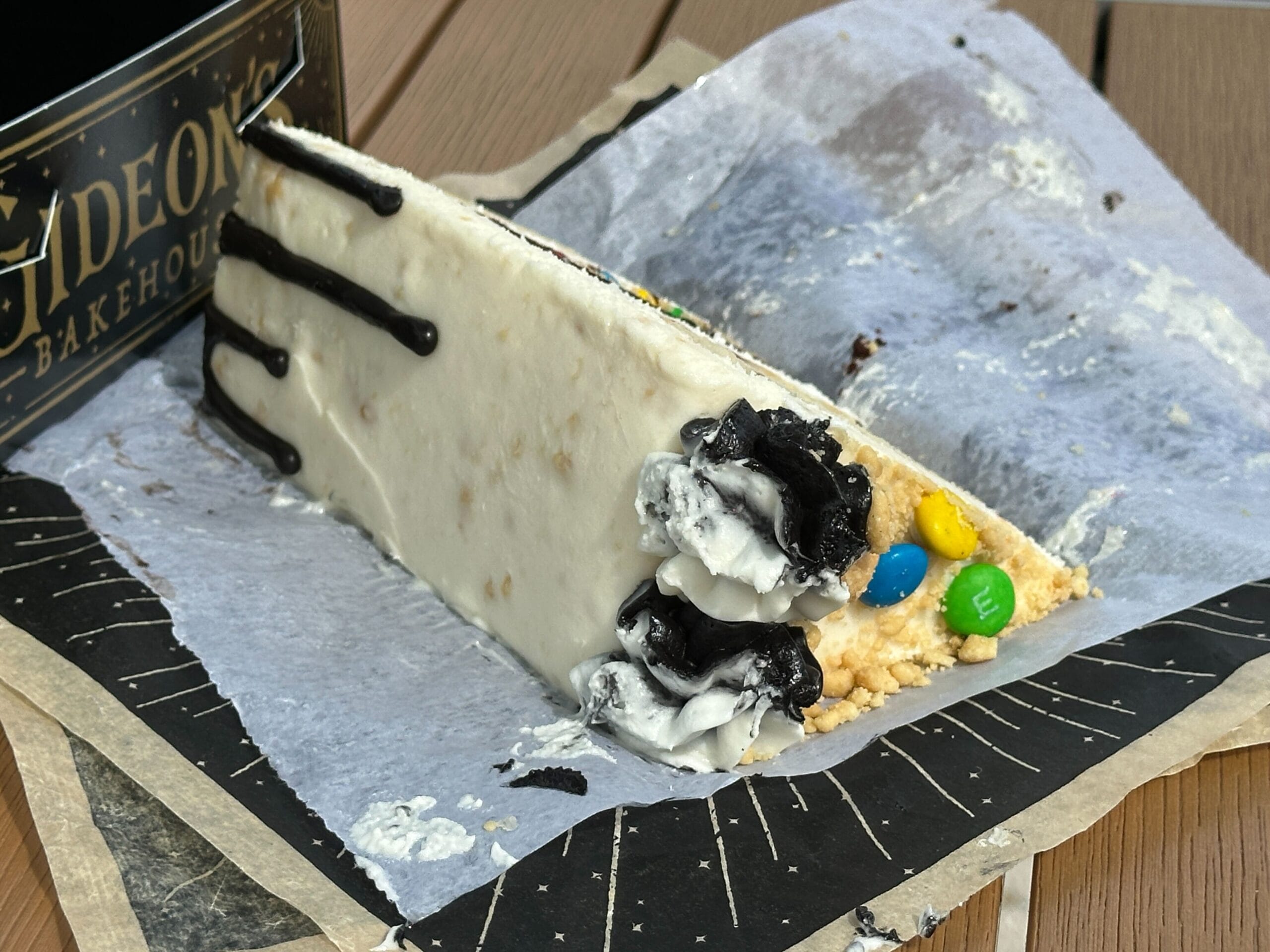 A slice of Gideon's Bakehouse Bride of Frankenstein Cake with black icing, Oreos, and M&Ms on parchment—no castle in sight here!