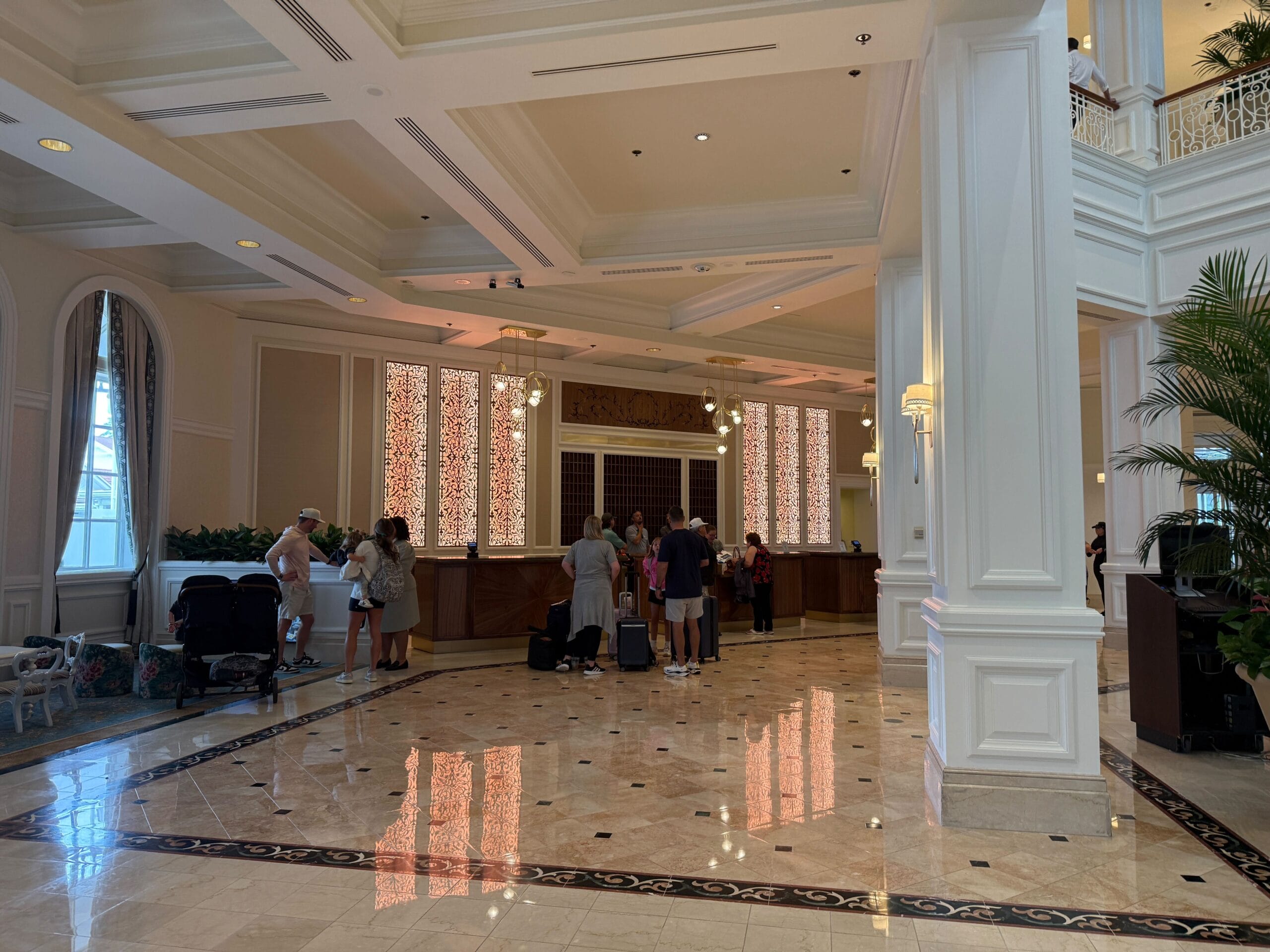 Hotel lobby with people checking in at the front desk, marble floors, and elegant white columns and decor.