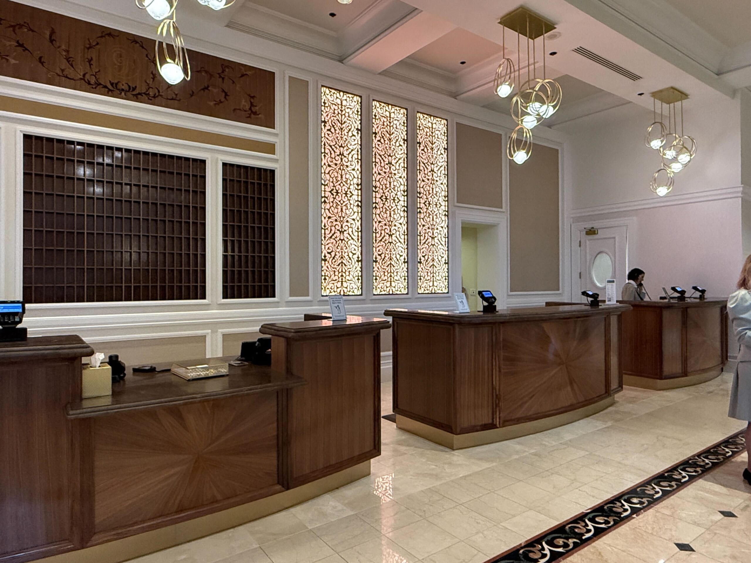 Hotel front desk area with wooden counters, decorative wall panels, and modern hanging lights.