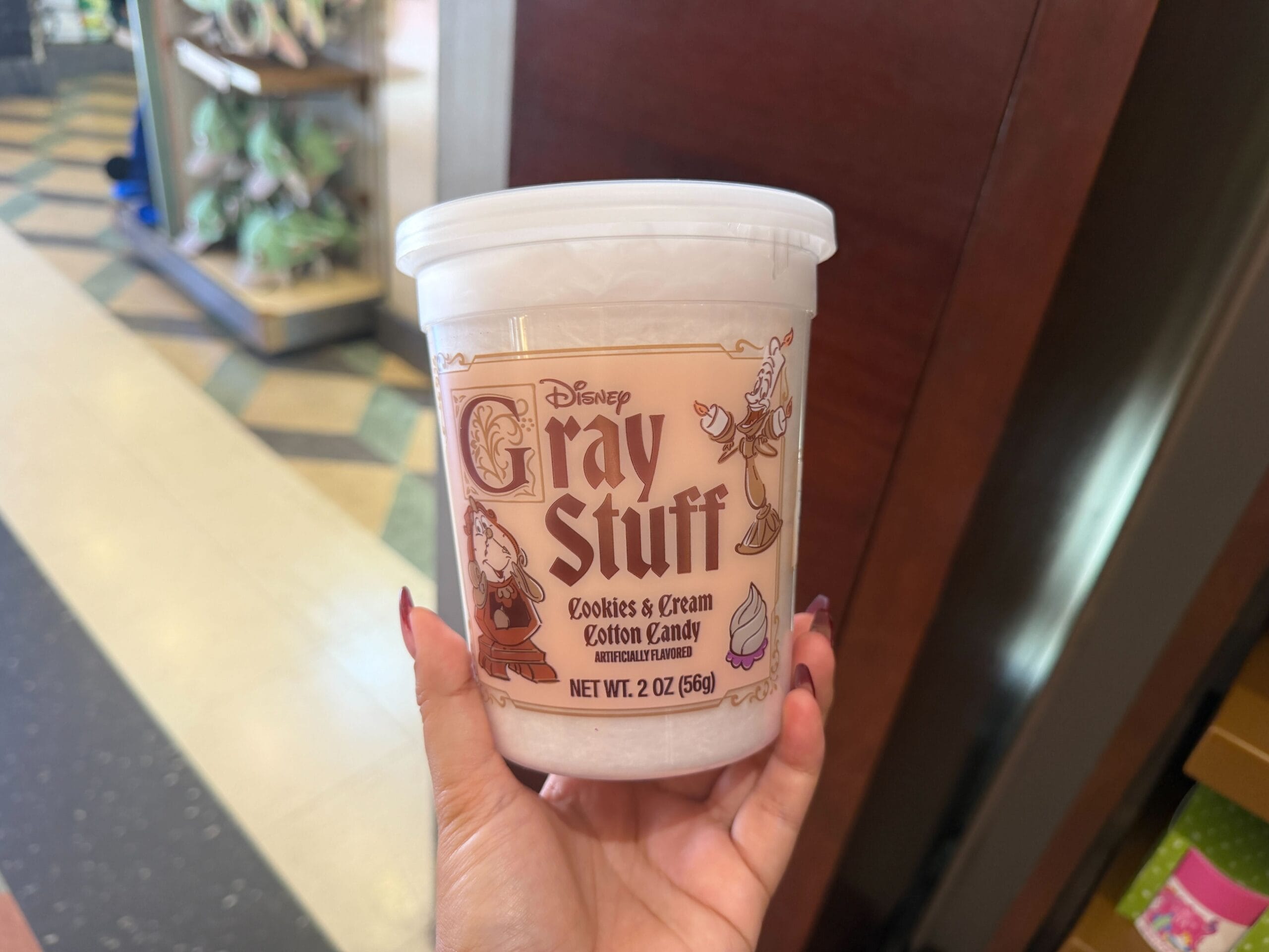 A hand holds Disney Gray Stuff Cookies & Cream Cotton Candy in a store, a treat inspired by Disney parks' whimsical desserts.