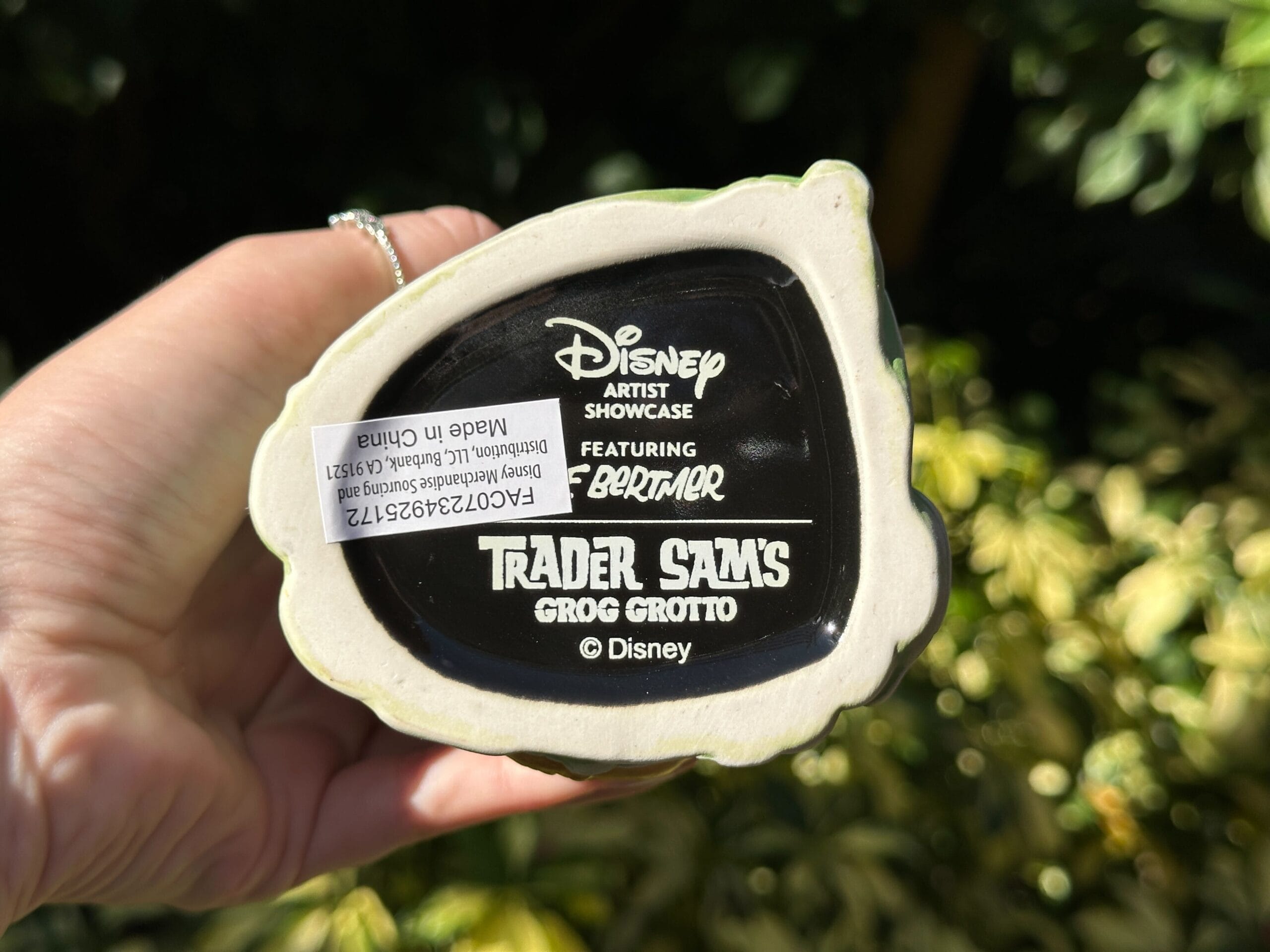 A hand displays a Trader Sam’s Grog Grotto mug base at Polynesian Village Resort, featuring Disney and Eekum Bookum logos.