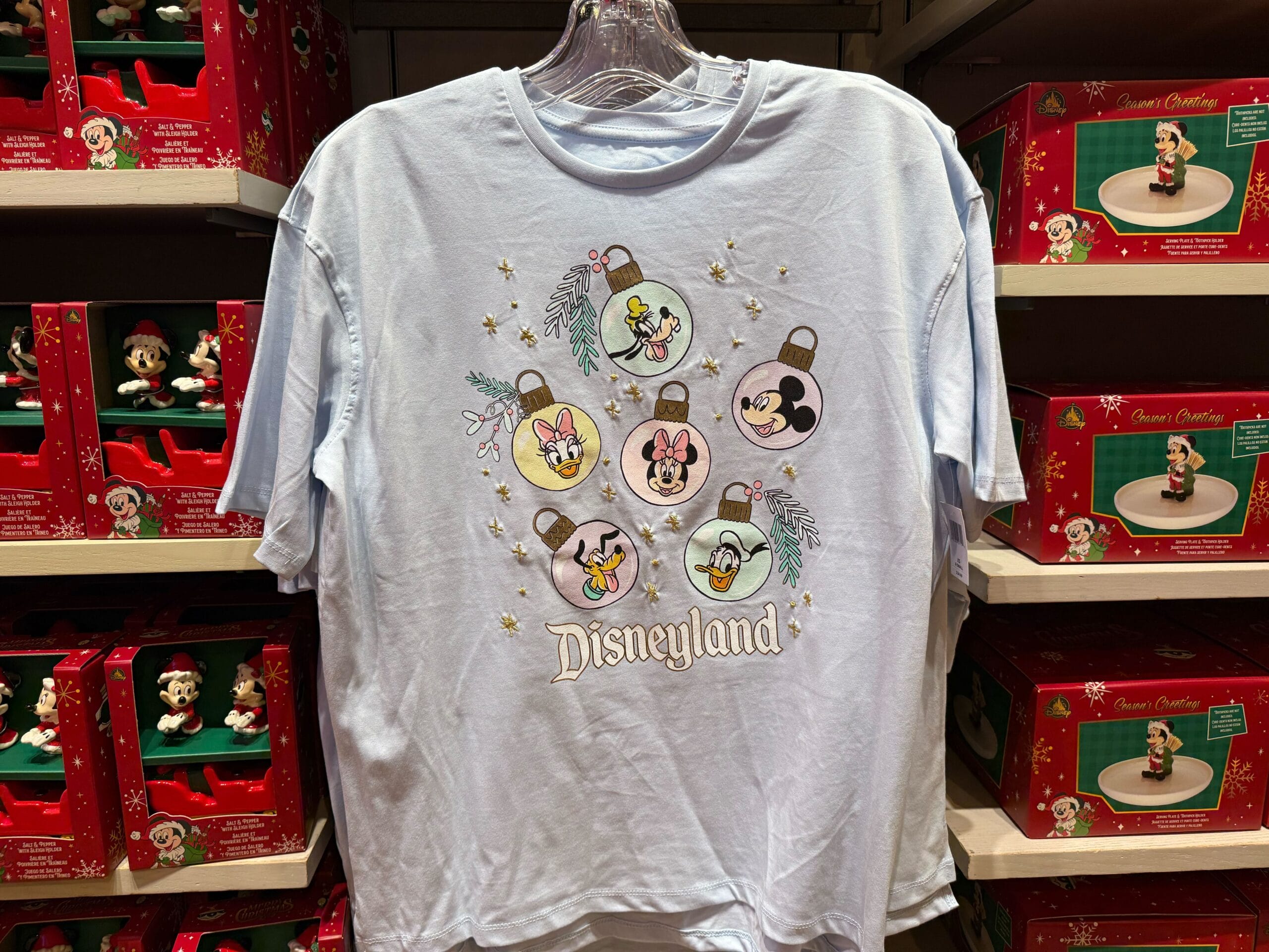 Light blue Disneyland Resort T-shirt with Disney character ornaments, displayed among holiday merchandise; no castle shown.