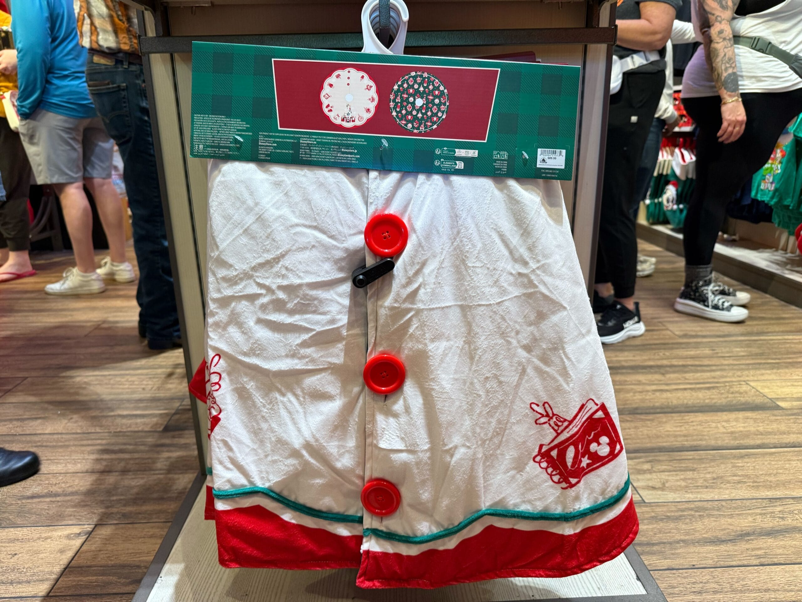 White holiday tree skirt with red accents, featured among festive Christmas merchandise at Disneyland Resort, inside a bustling shop.