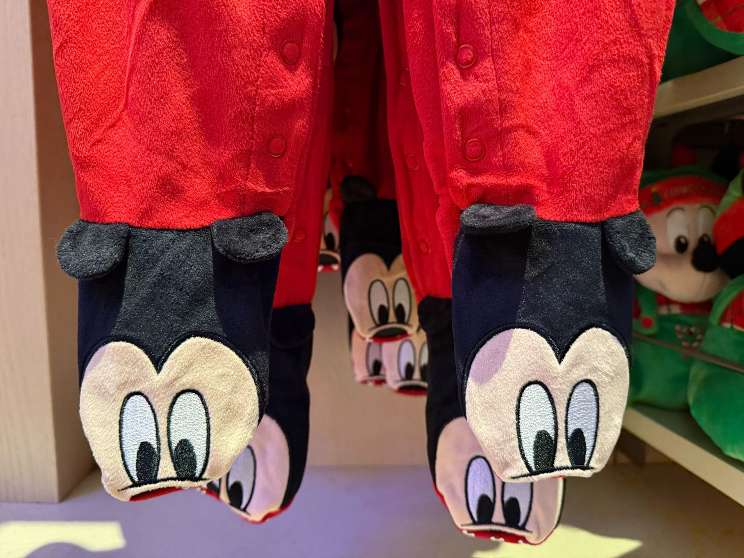 Red pajamas with attached slippers showing cartoon faces, part of Disneyland Resort’s Christmas merchandise—not WDW castle theme.