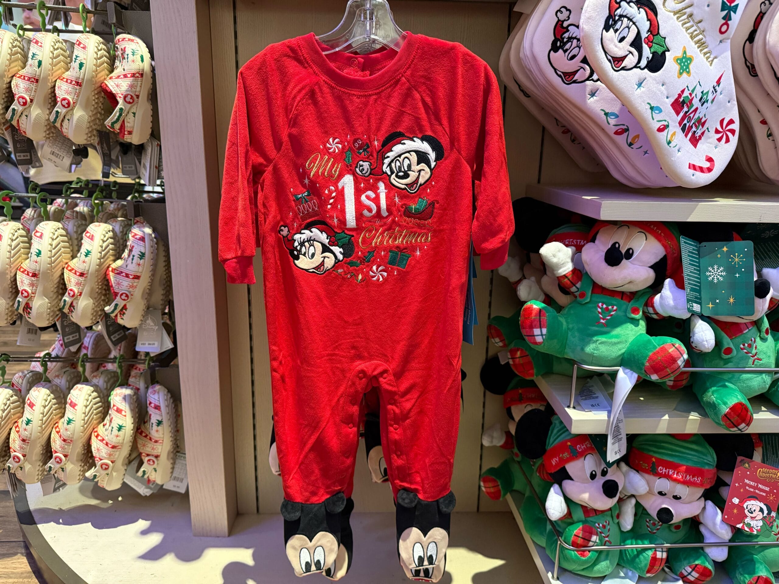 Red "My 1st Christmas" Mickey Mouse baby onesie displayed with Disneyland Resort holiday merchandise, no castle in view.