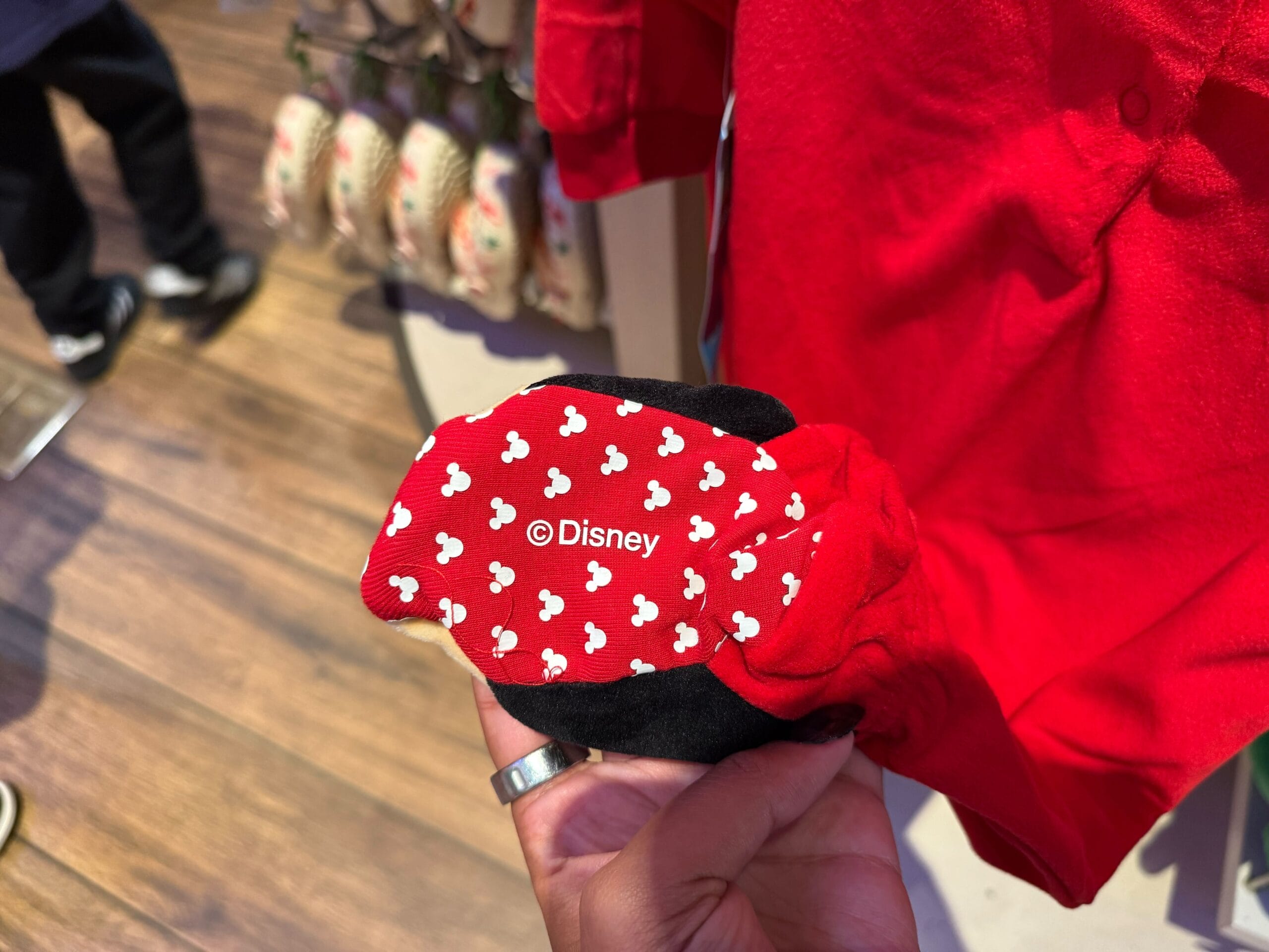 A hand holds a red Disneyland Resort item with white Mickey heads, festive like park Christmas merch. No castle seen to compare.
