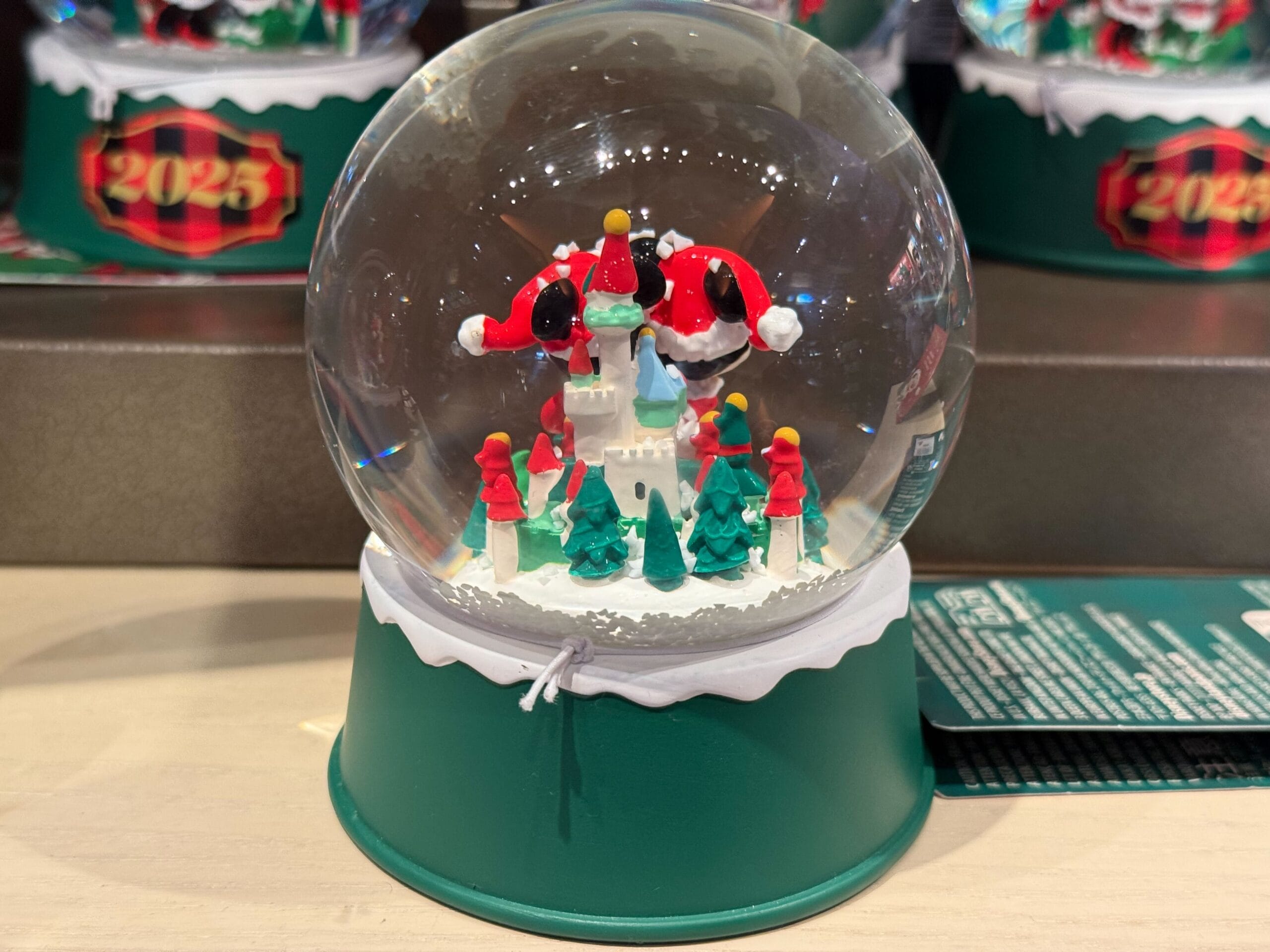 A Christmas snow globe with Santa, trees, "2024," and a castle resembling Sleeping Beauty Castle at Disneyland on a green base.