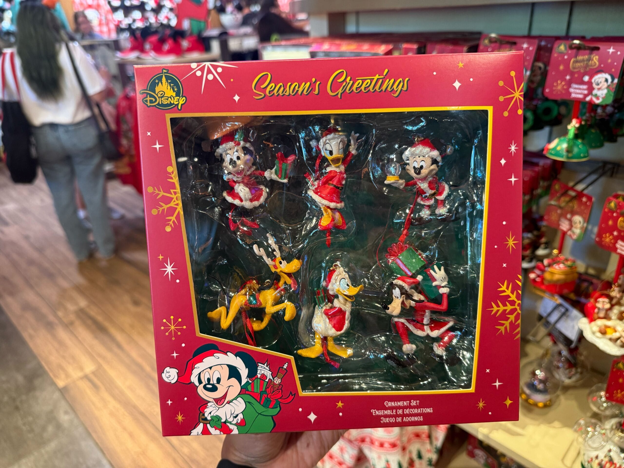 A hand holds a boxed set of Disney Christmas ornaments at Disneyland Resort, with fan-favorite characters—no castle in this image.