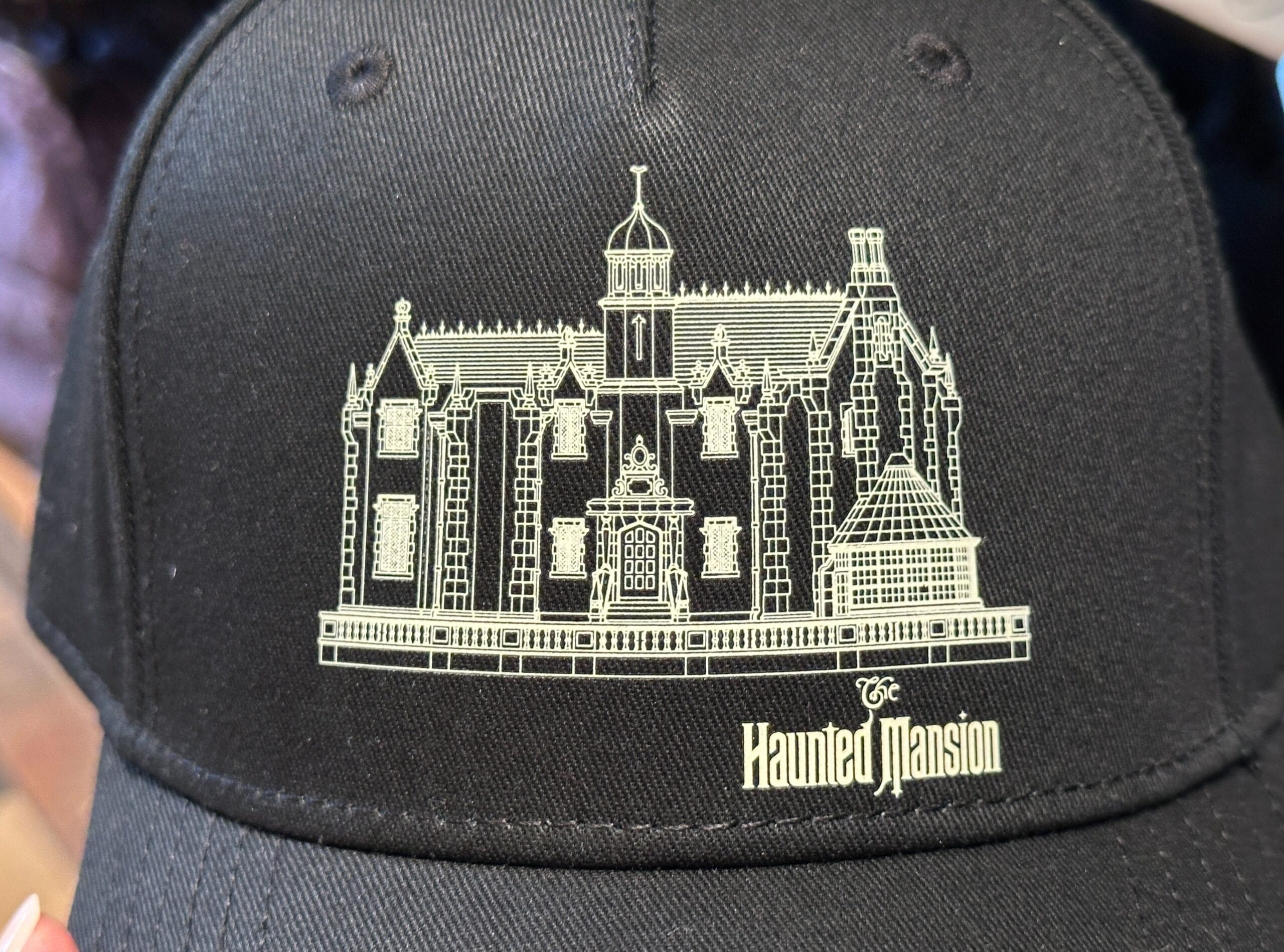 Black hat featuring a white outline of the Haunted Mansion from Disney Parks, with "The Haunted Mansion" text below the iconic facade.