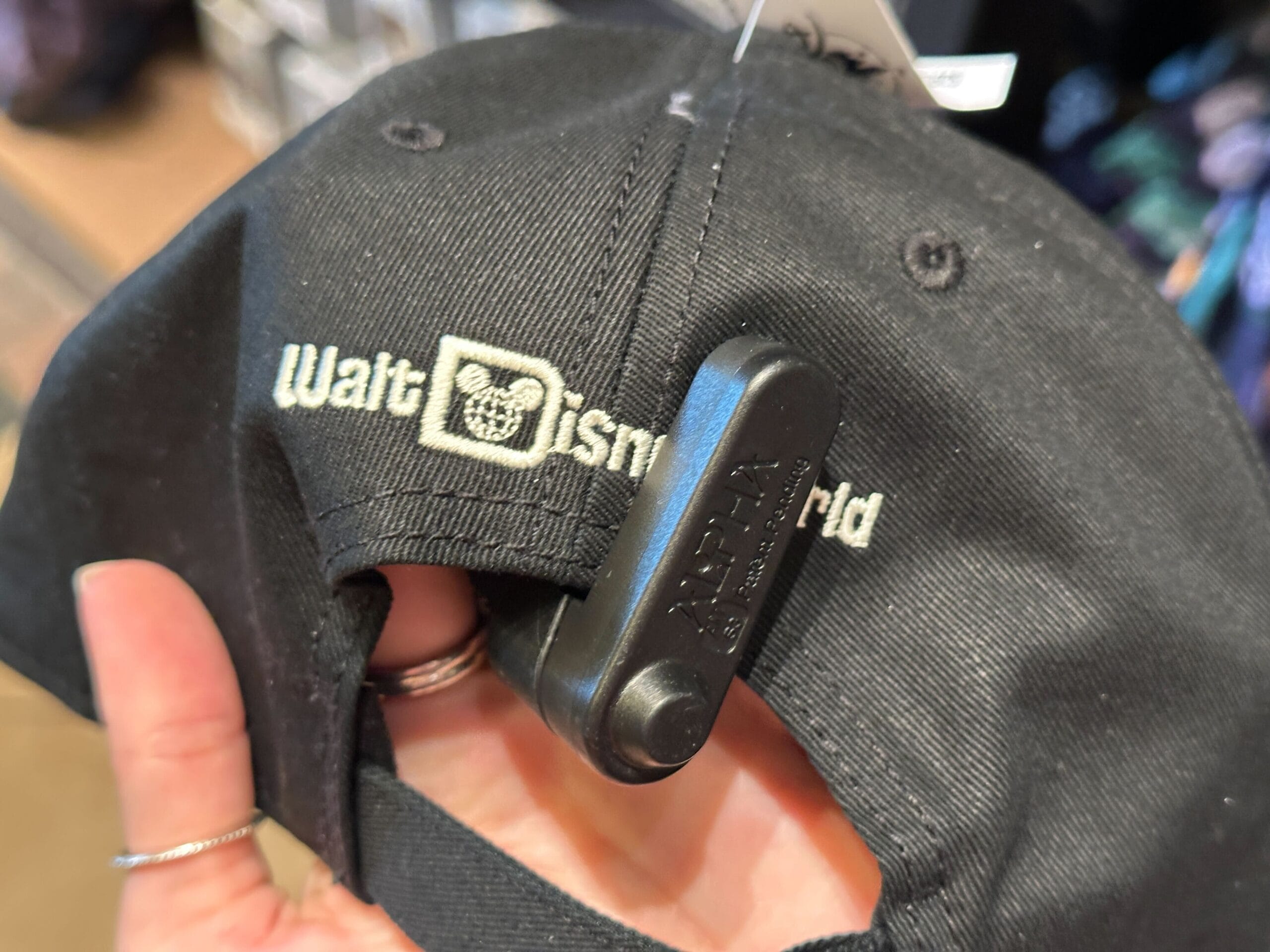 Close-up of a hand holding a black Walt Disney World hat with a security tag, likely purchased at one of the Disney parks.