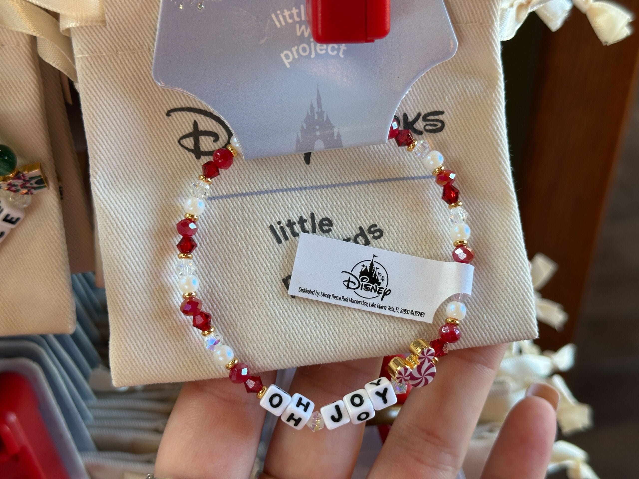 A beaded bracelet with red, white, and gold beads spells out "OH JOY" in block letters—like a cheerful Disney souvenir.