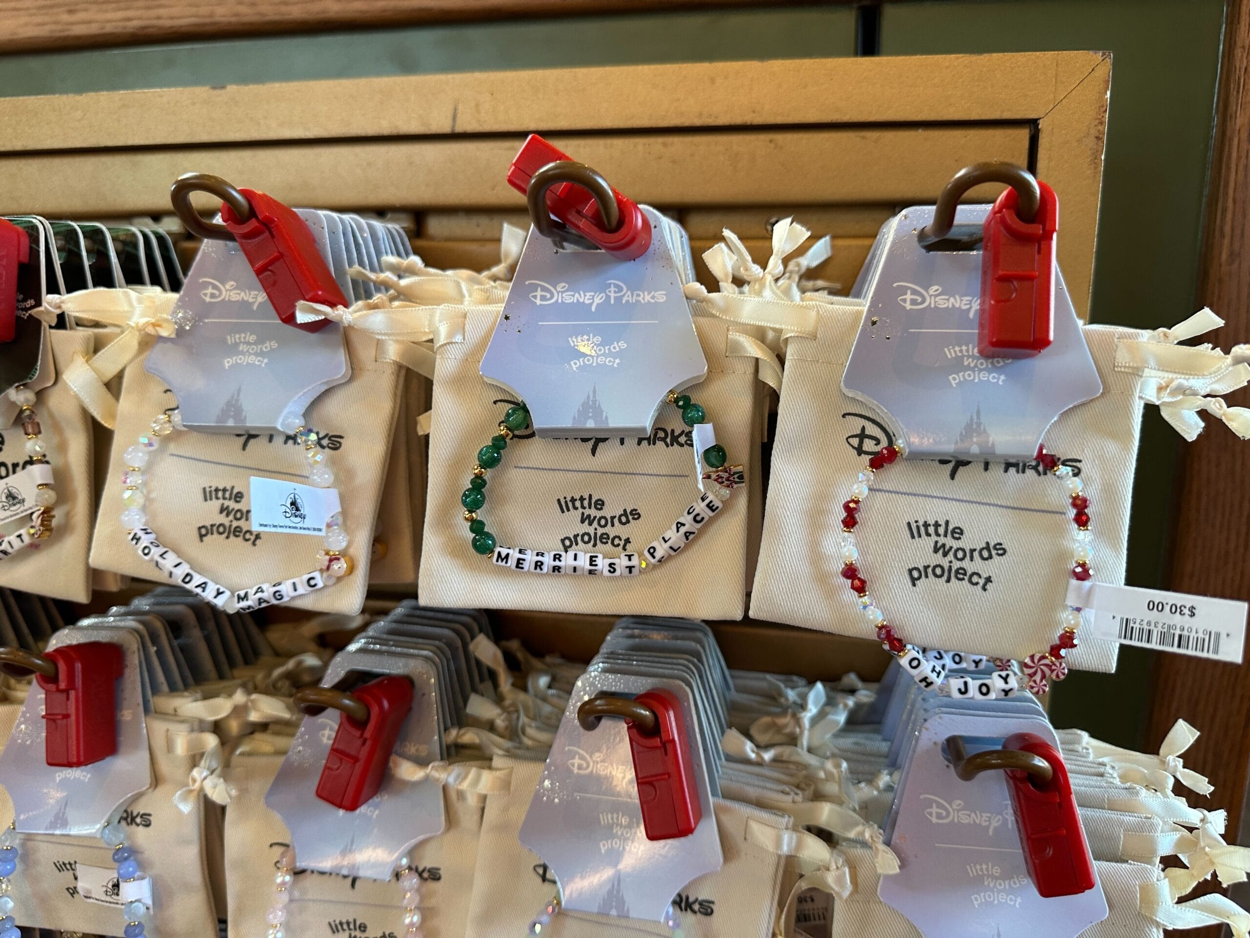 Beaded bracelets from Disney Parks with letter blocks spelling phrases hang on hooks with price tags, reminiscent of Main Street shops.