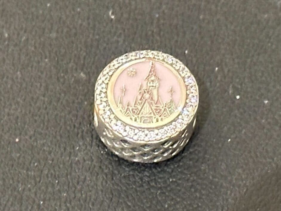 A small, round, silver-colored object with a pink top sits on a textured dark surface, reminiscent of Disney park souvenir details.