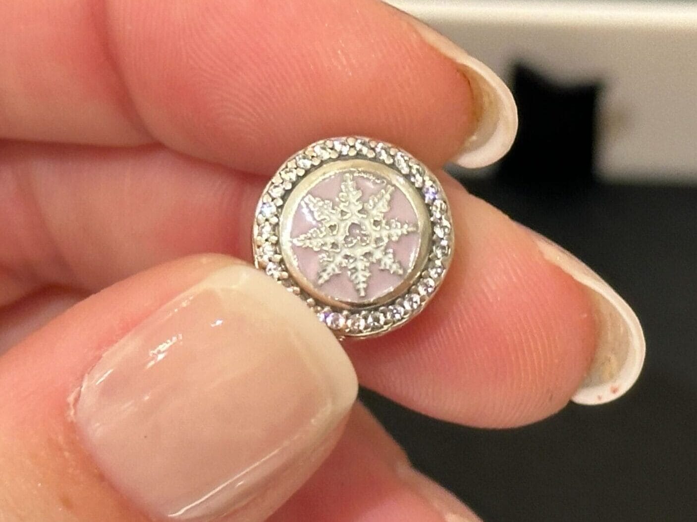 A hand holds a round charm with a star design and sparkling crystals, reminiscent of Disney park jewelry found at gift shops near Cinderella Castle.