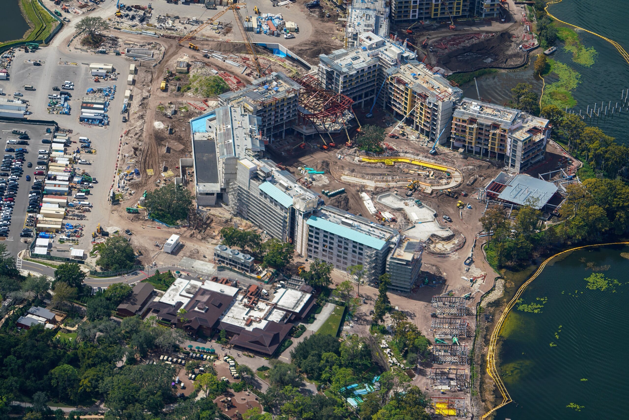 Aerial view of a Disney park construction area with several buildings, a parking lot, and water—no castle like Disney’s icons visible.
