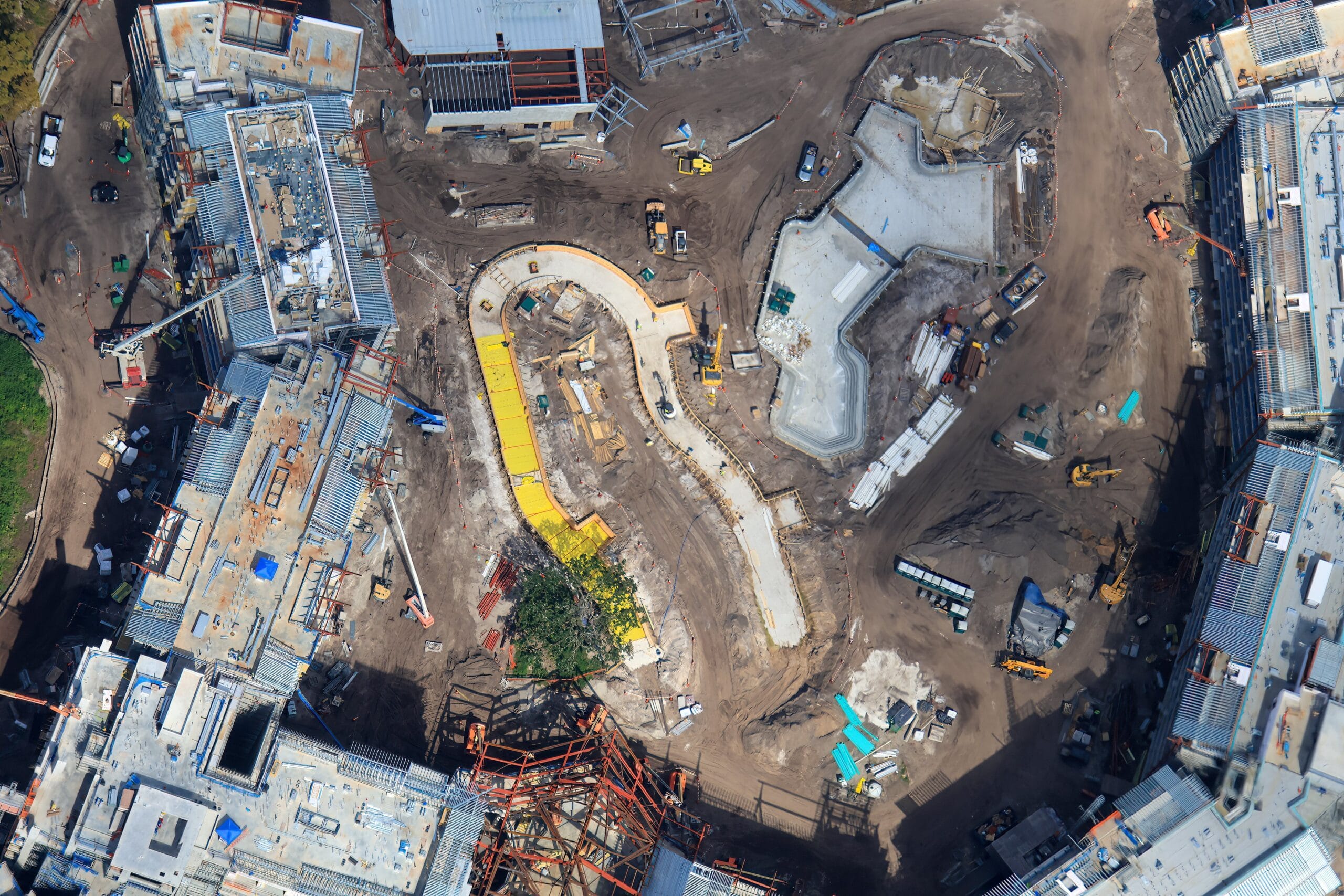 Aerial view of a construction site in a Disney park with buildings, winding paths, machinery, and materials—no castle visible.