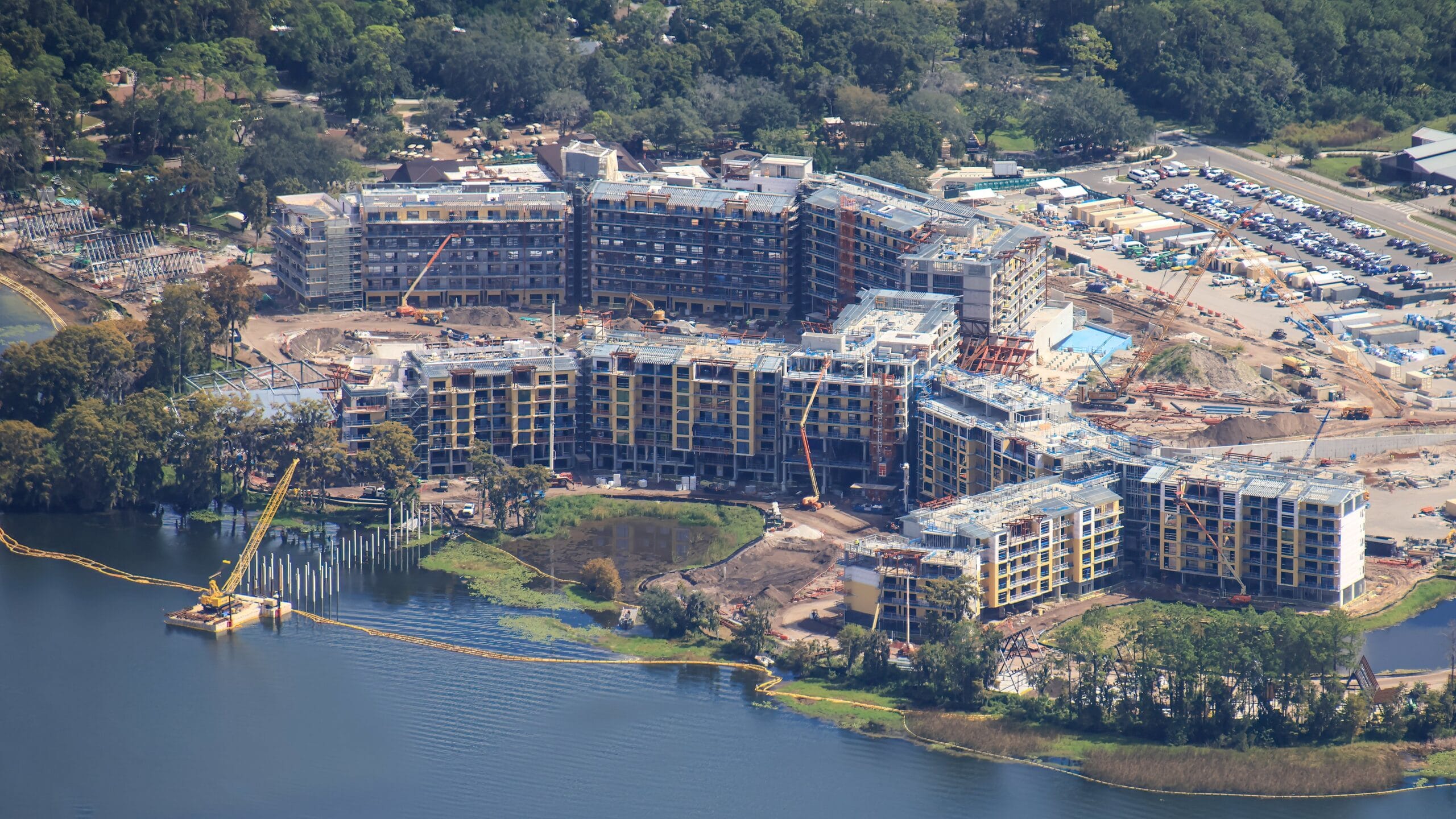 Aerial view of a large lakeside building under construction, surrounded by trees and equipment, similar to Disney resort projects.