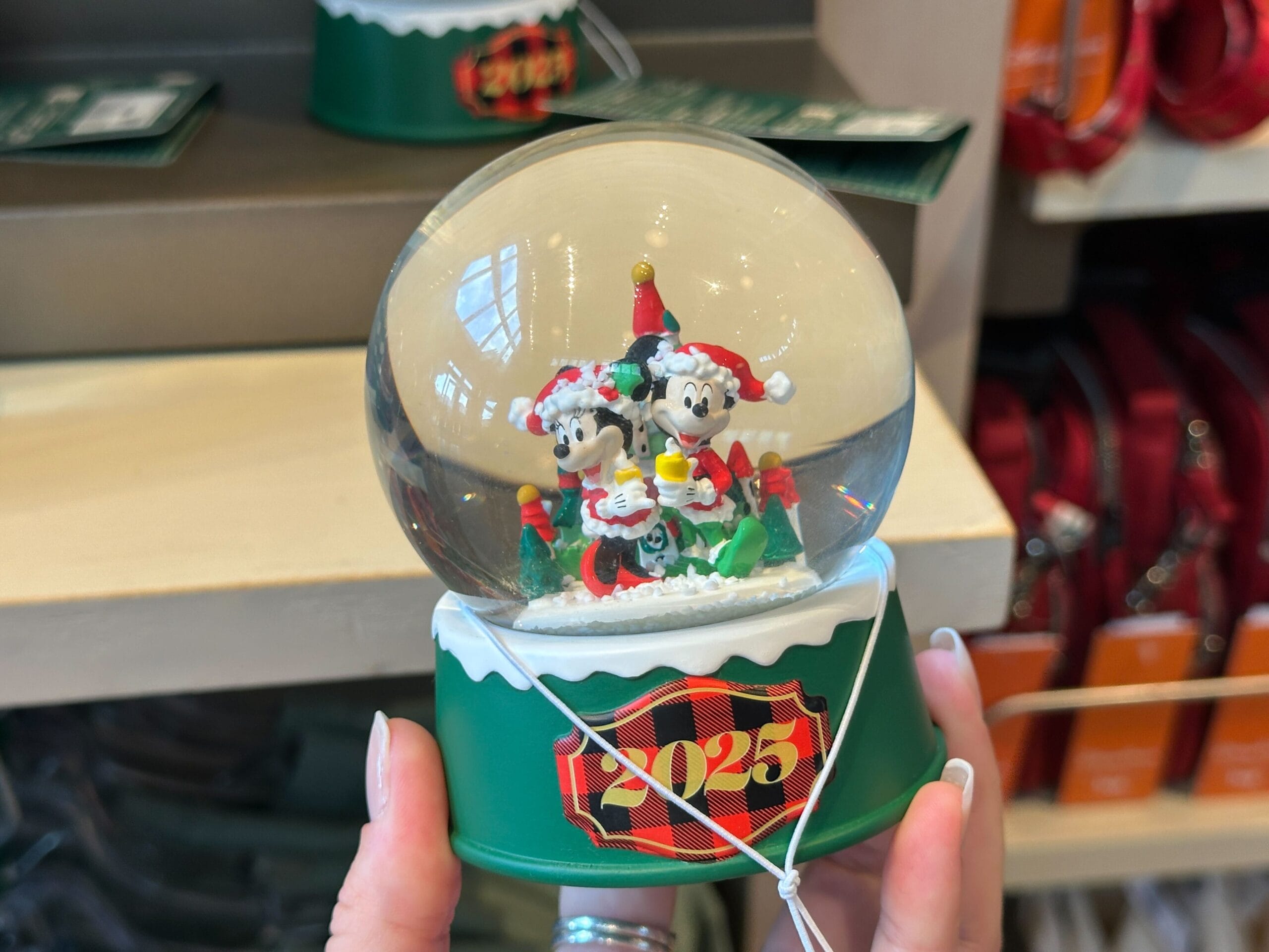 Hand holding a 2025 snow globe featuring Mickey and Minnie in festive attire, reminiscent of Disney Parks holiday merchandise.