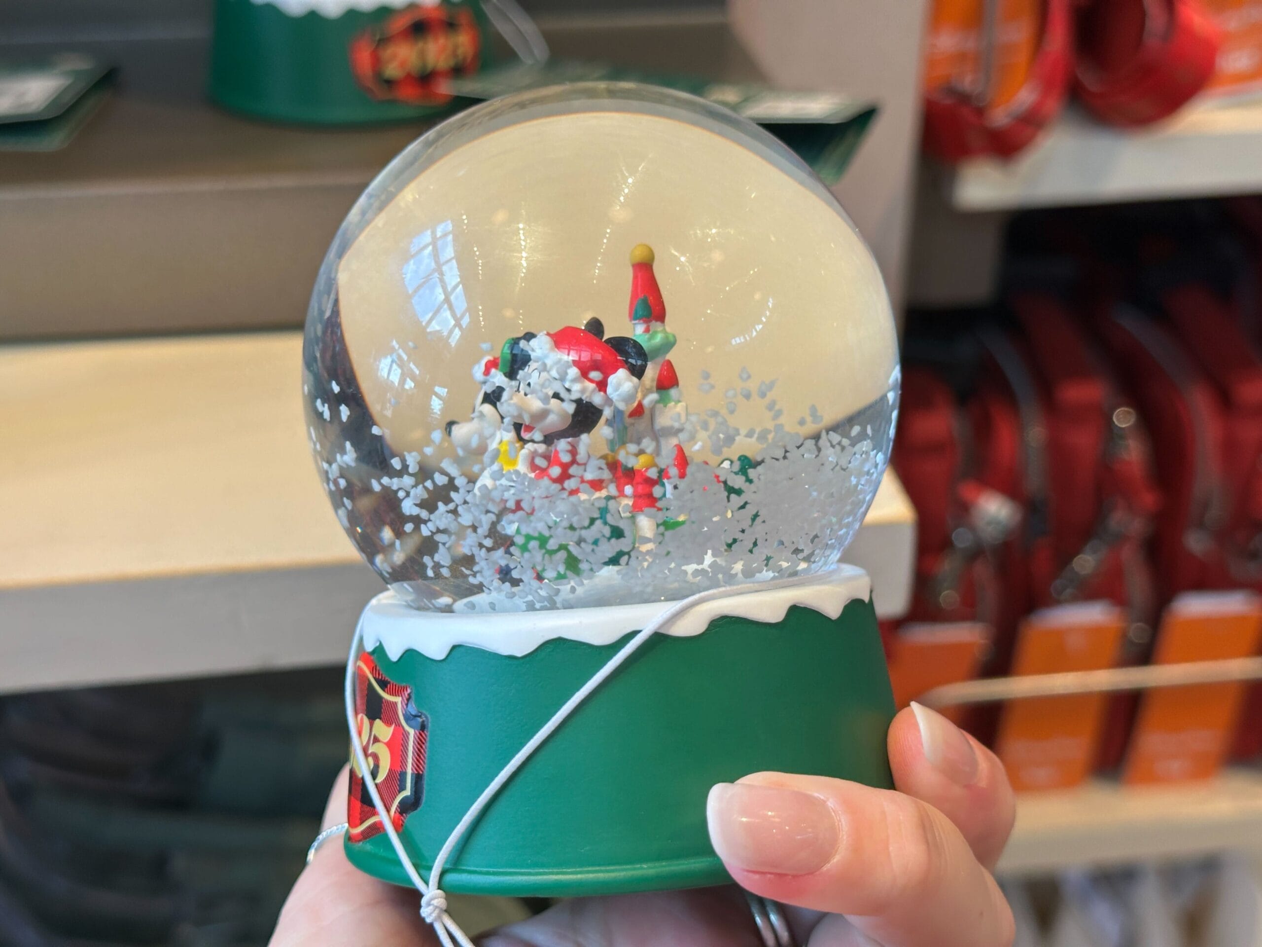 Hand holding a snow globe featuring a festive Santa Claus inside, on a green base with holiday icons, reminiscent of Disney park souvenirs.