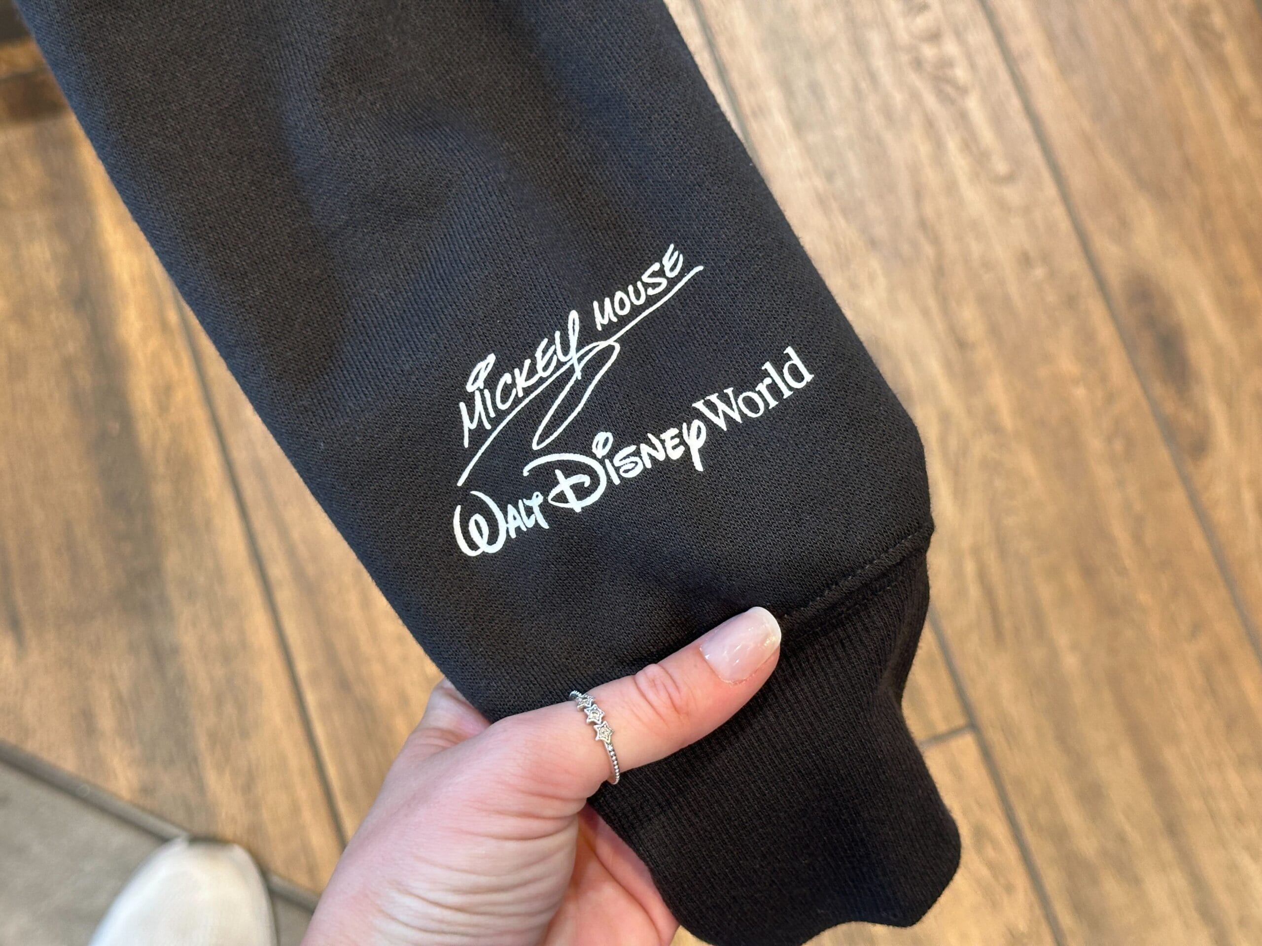 A hand holds a black sleeve with "Mickey Mouse Walt Disney World" in white, referencing the iconic Florida park near Cinderella Castle.