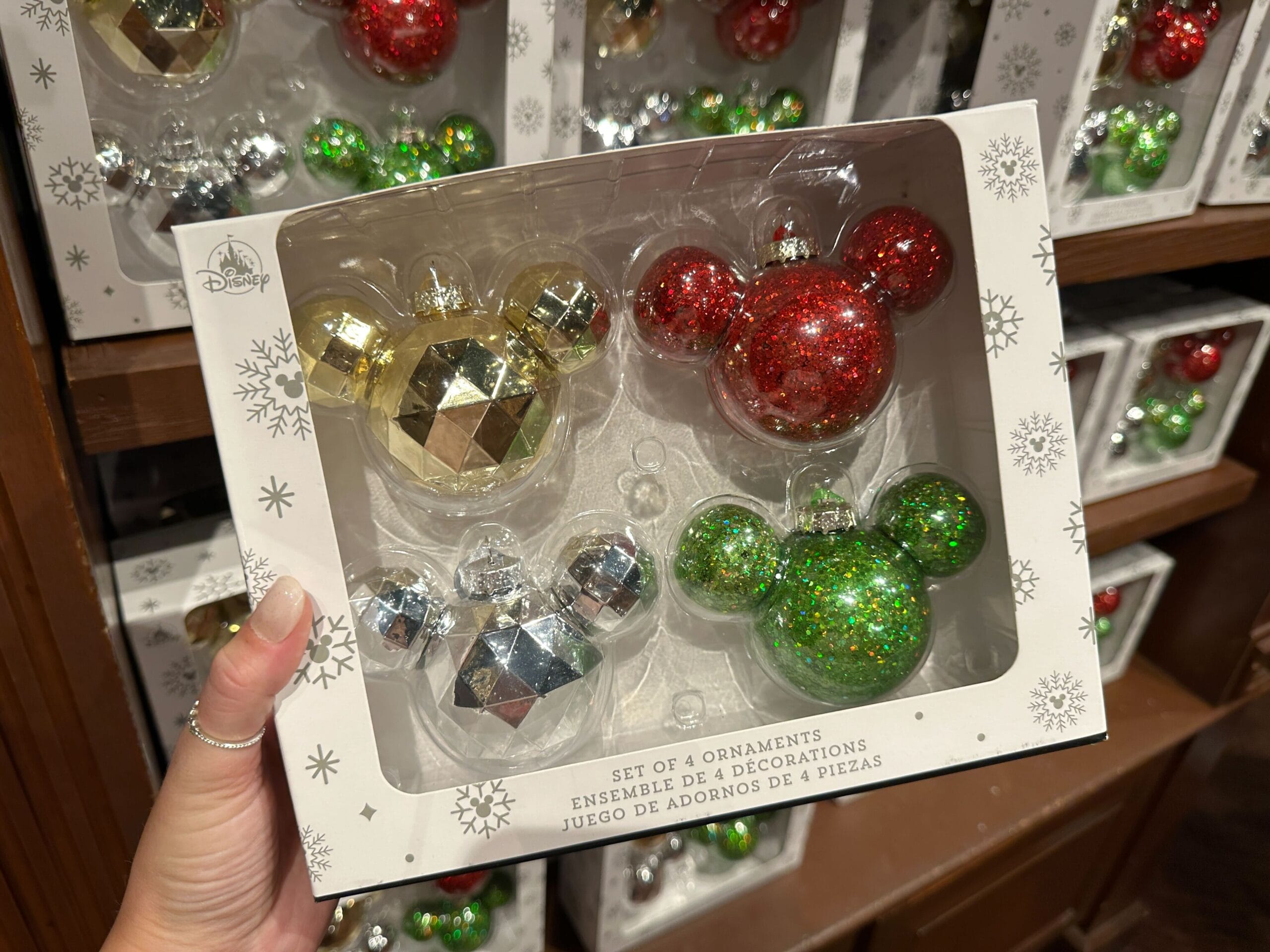 Hand holding a box of four Disney World Holiday Ornaments shaped like Mickey Mouse in festive colors.