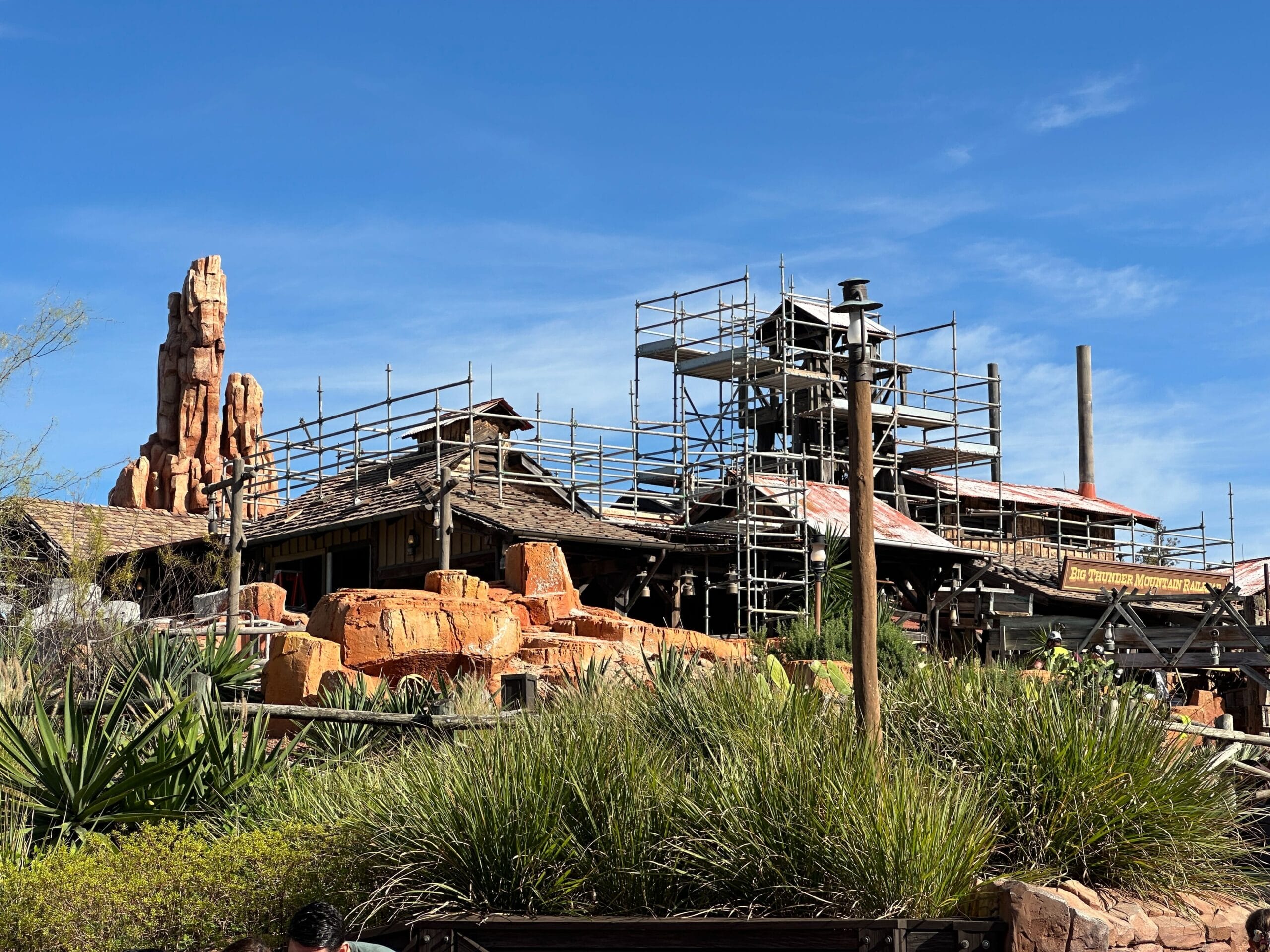 Scaffolding surrounds a western-themed Disney park ride under construction, with desert rocks and plants, like Frontierland.