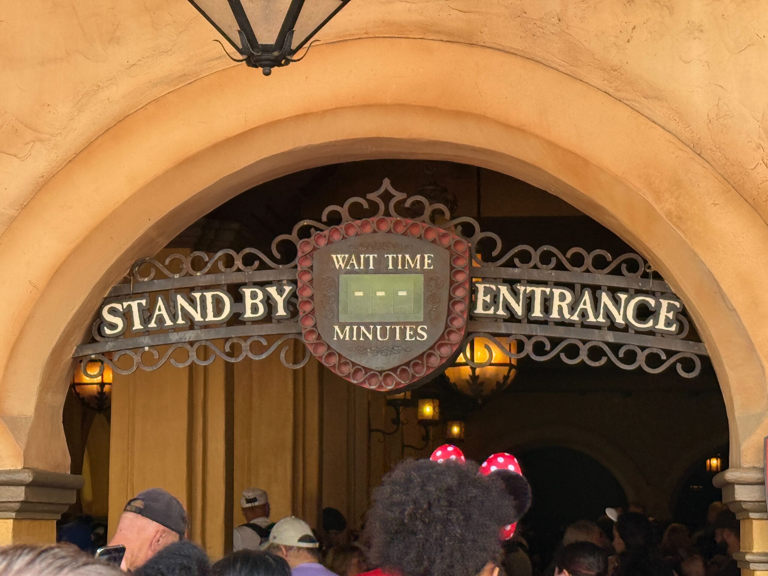 A "Stand By Entrance" sign with no wait time posted overlooks guests gathering at the entrance of a Disney park attraction.