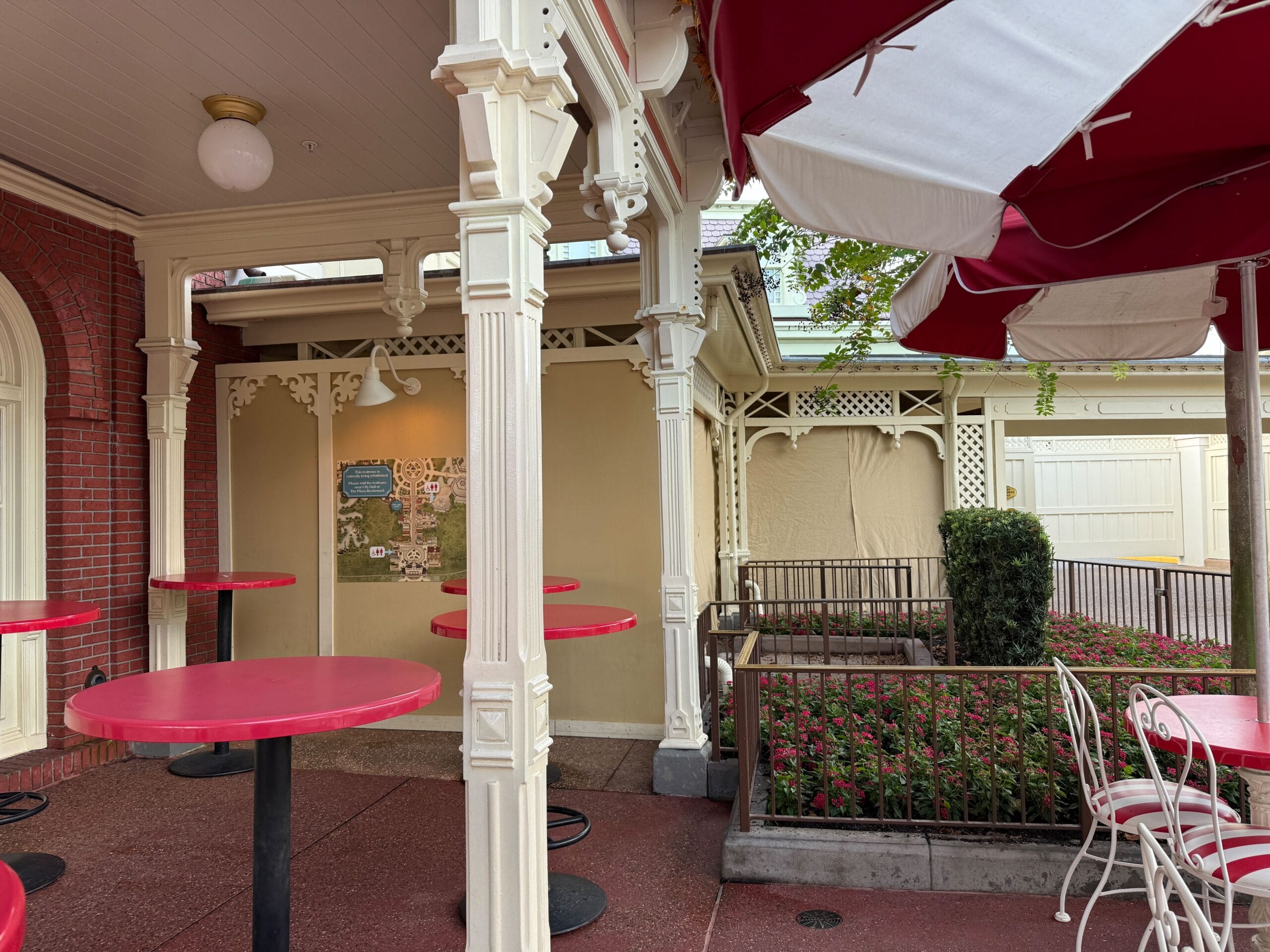Casey’s Corner patio at Magic Kingdom with red tables, white chairs, and umbrellas near a construction wall and vibrant flowerbeds.