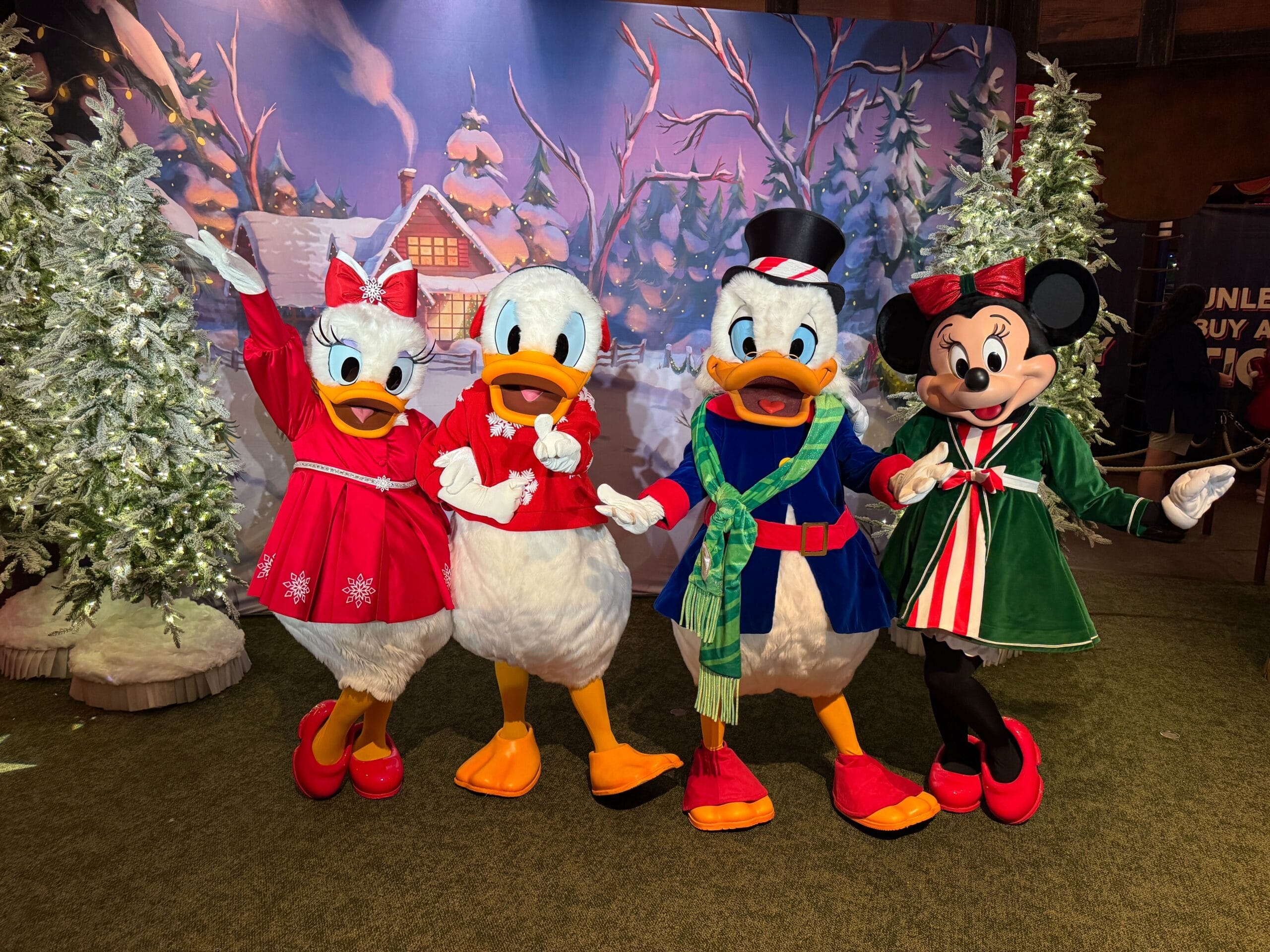 Daisy, Donald, Scrooge, and Minnie in festive attire at Magic Kingdom, snowy trees and cabin in the background.