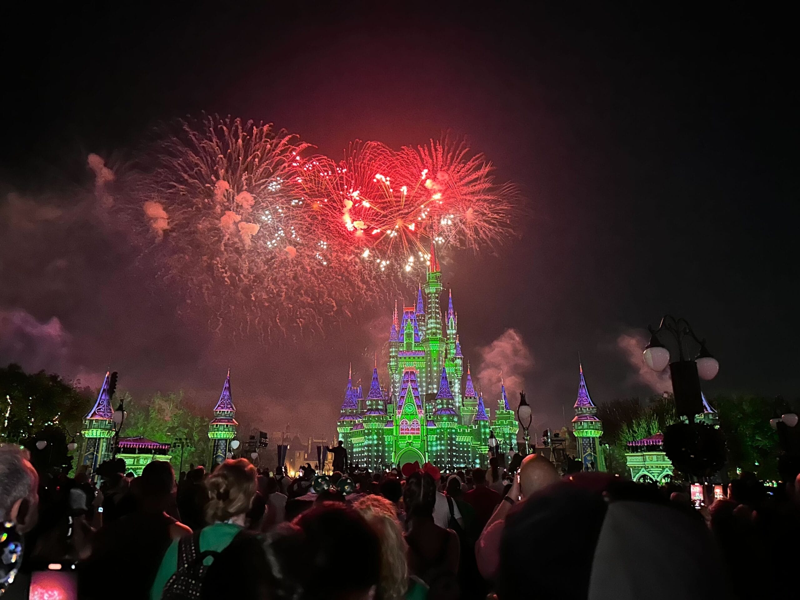 Vivid fireworks light up the night sky above Cinderella Castle, Magic Kingdom’s iconic centerpiece, as holiday projections color it a vibrant green.