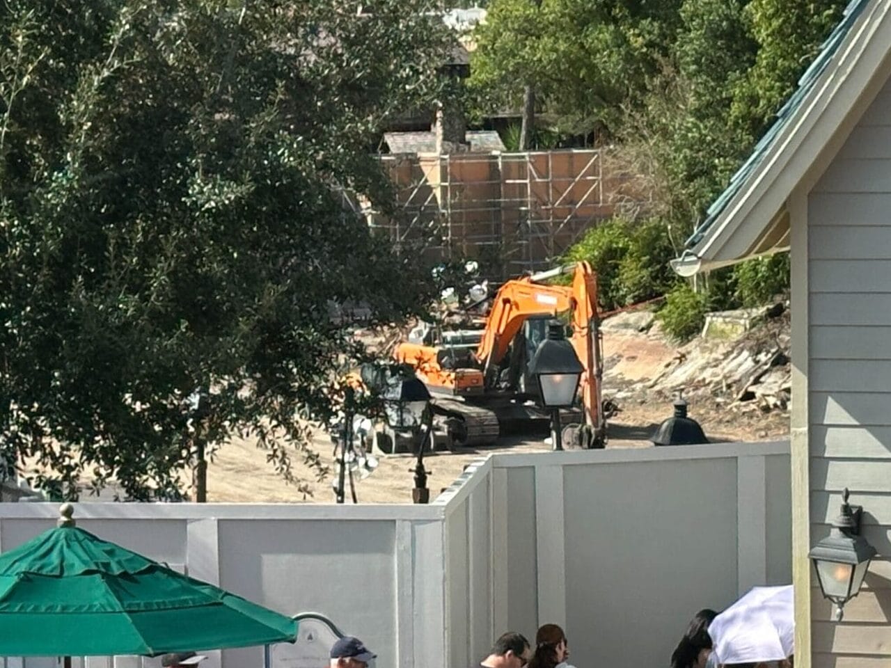 Guests queue near a construction site with an excavator behind a white fence in a Disney park area.