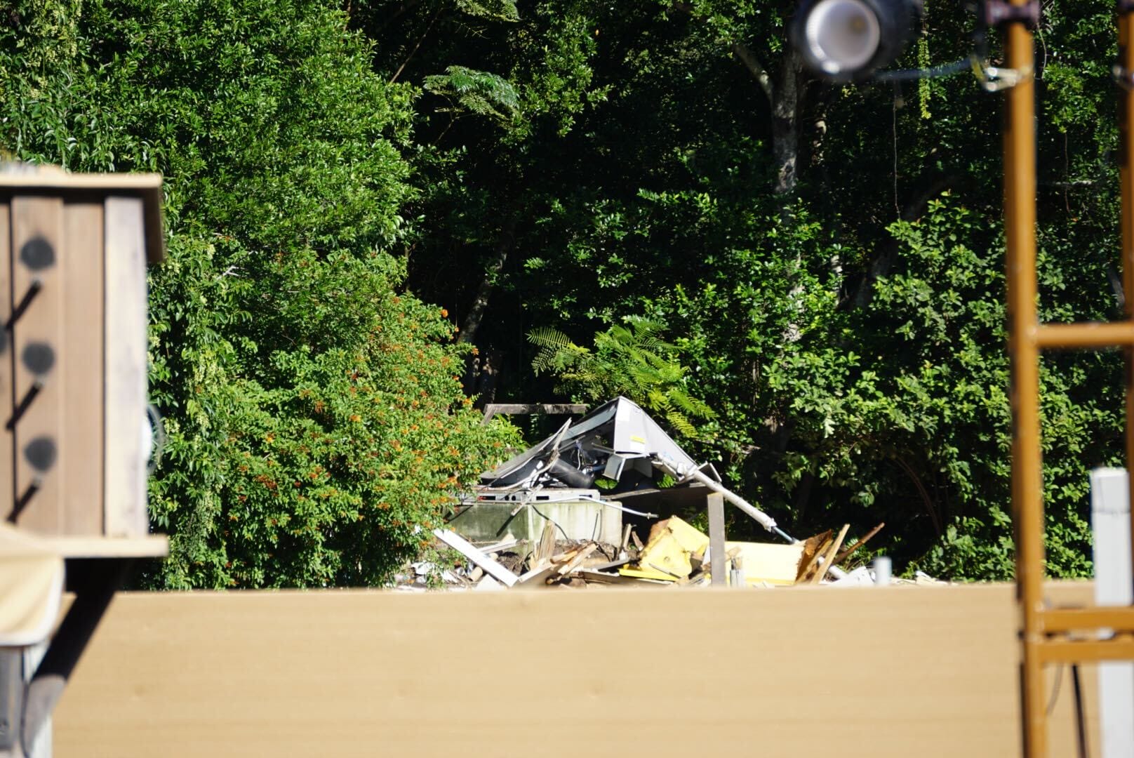 A partially collapsed roof and debris lie among lush trees, construction materials in front—no resemblance to Disney park castles.