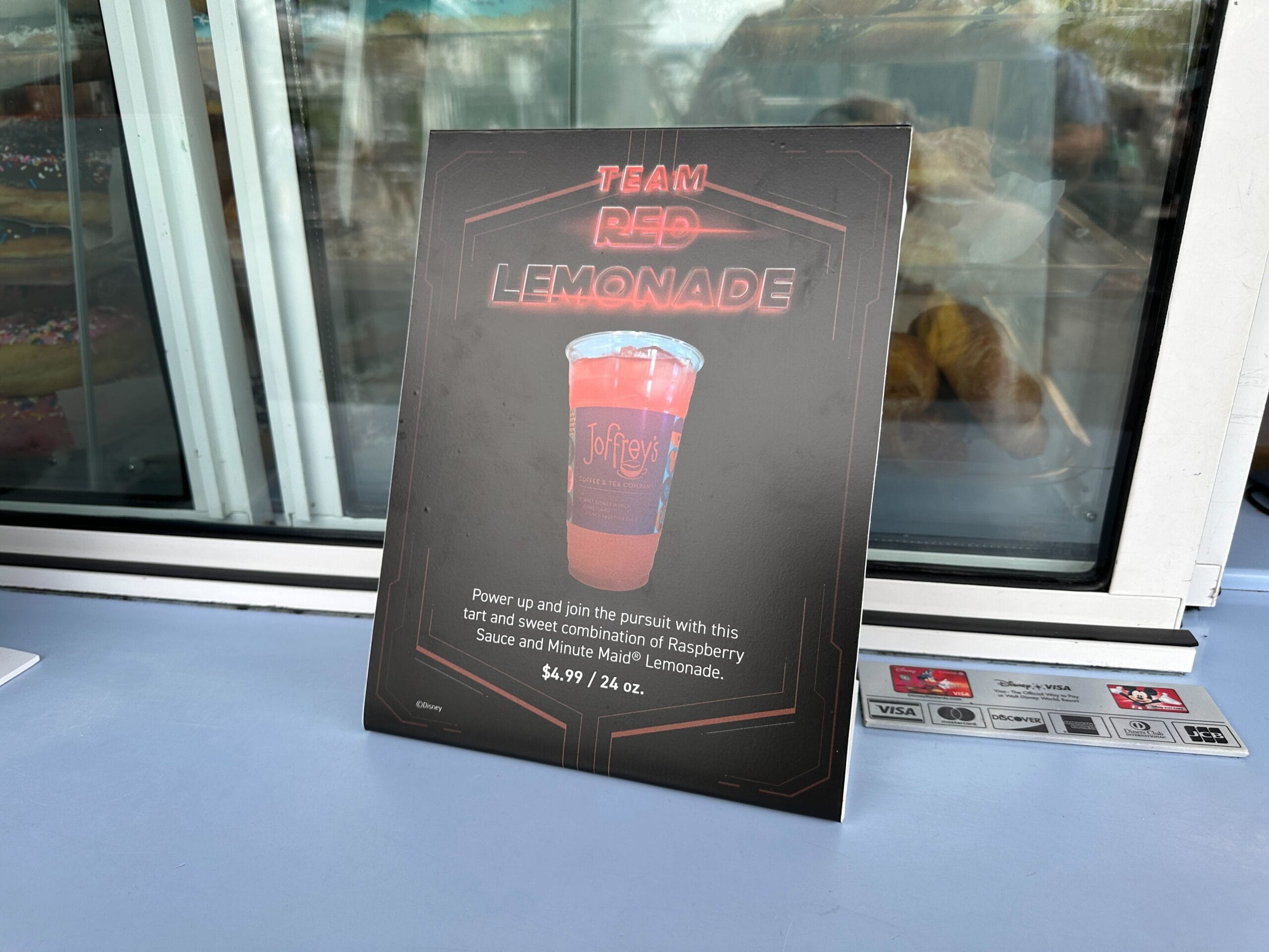 A Walt Disney Park counter sign promotes "Team Red Lemonade," a raspberry-Minute Maid drink, for $4.99. No castle is seen.