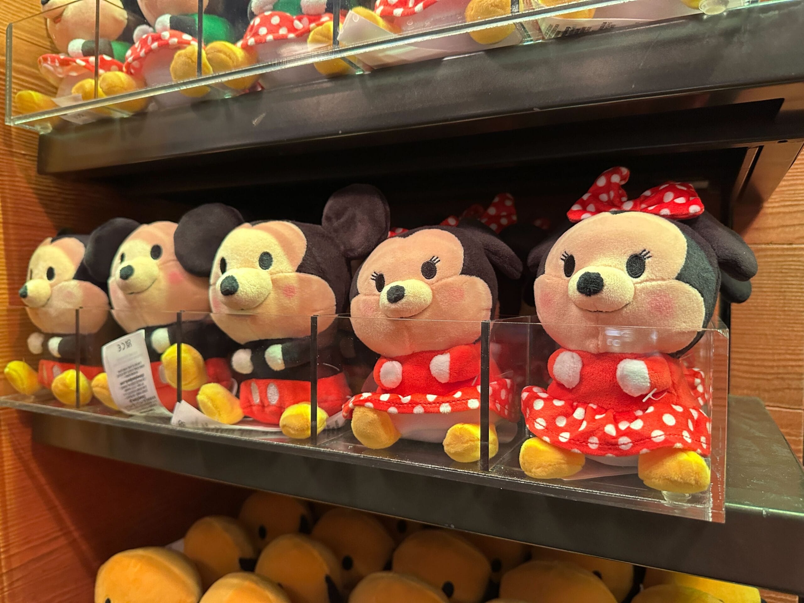 Plush Minnie Mouse dolls in classic red polka dot dresses and bows lined up on a Disney park store shelf, ready for visitors.