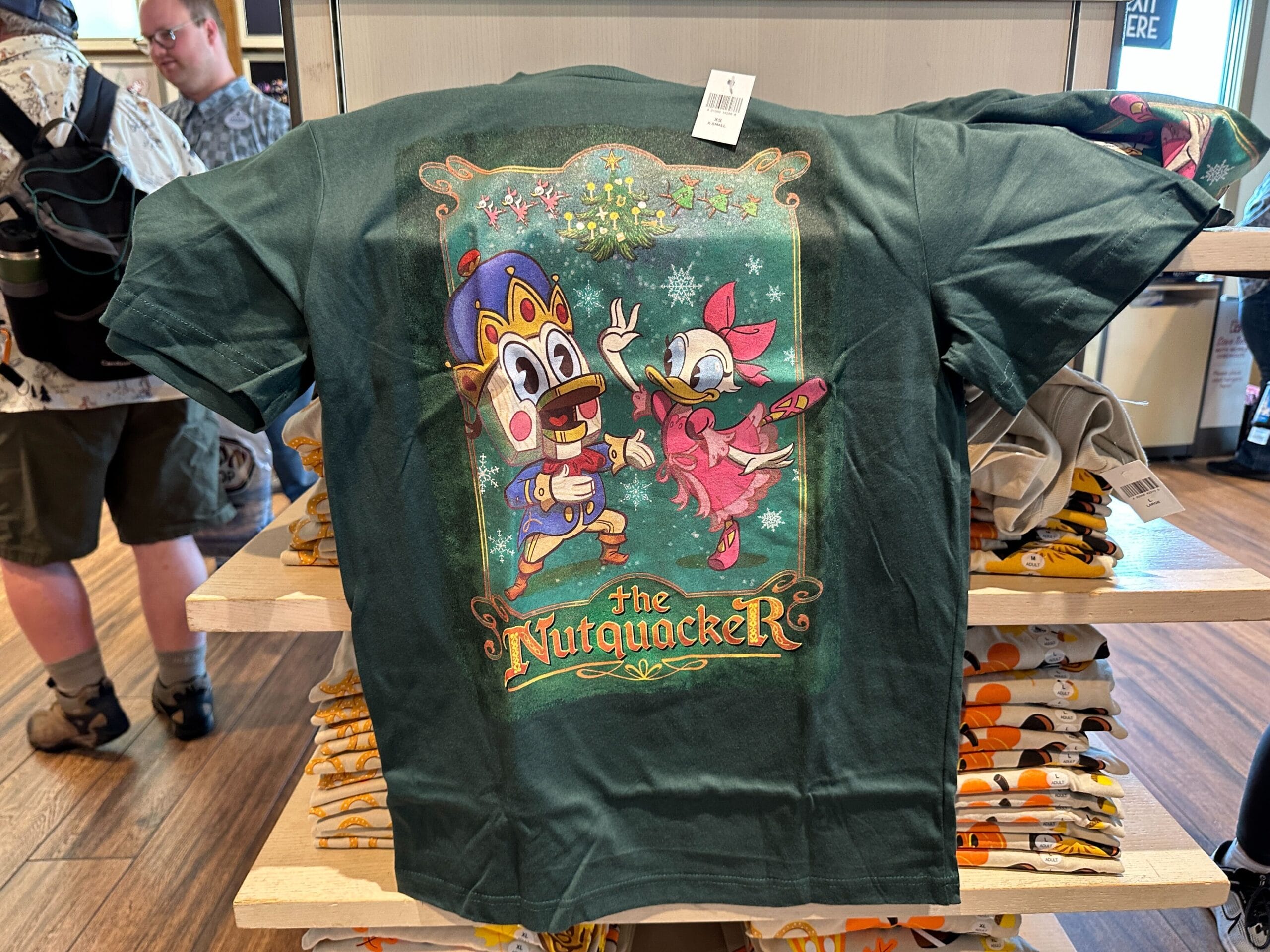 Green tee with Donald and Daisy Duck as Nutcracker characters, "The Nutquacker" text—festive Disney Parks holiday merchandise.