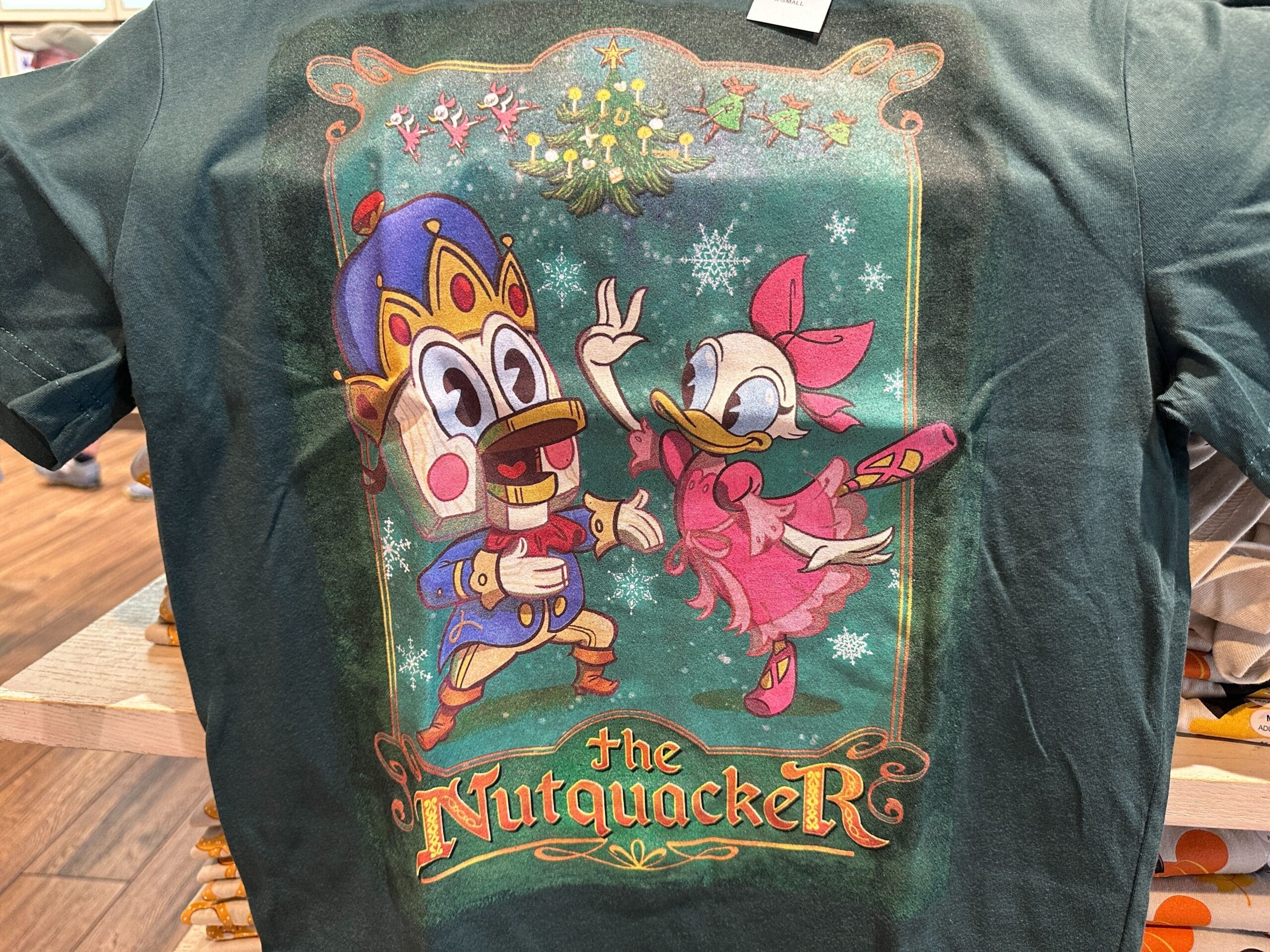 A T-shirt featuring cartoon ducks as Nutcracker and ballerina, titled "The Nutquacker," with a festive background, reminiscent of Disney park holiday apparel.