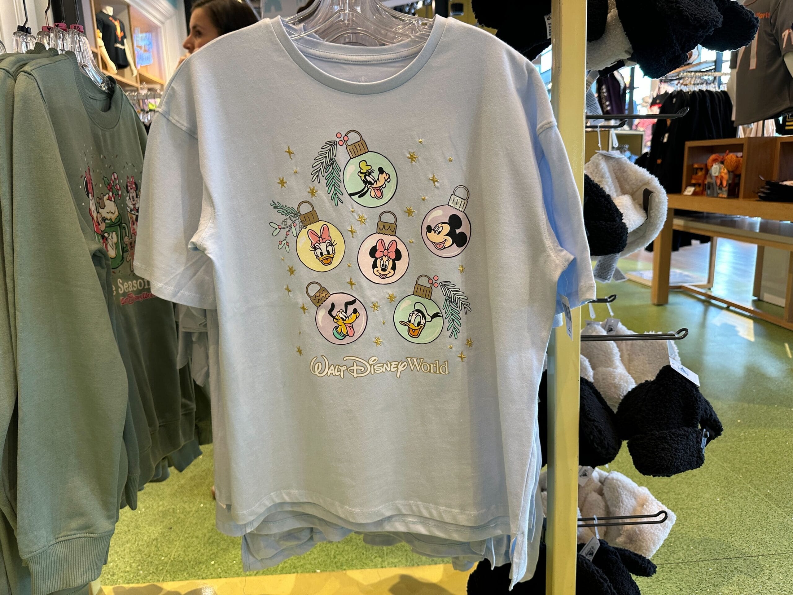 Light blue Disney World Holiday Shirt with character ornaments and holiday text, seen in Animal Kingdom shop, no castle visible.