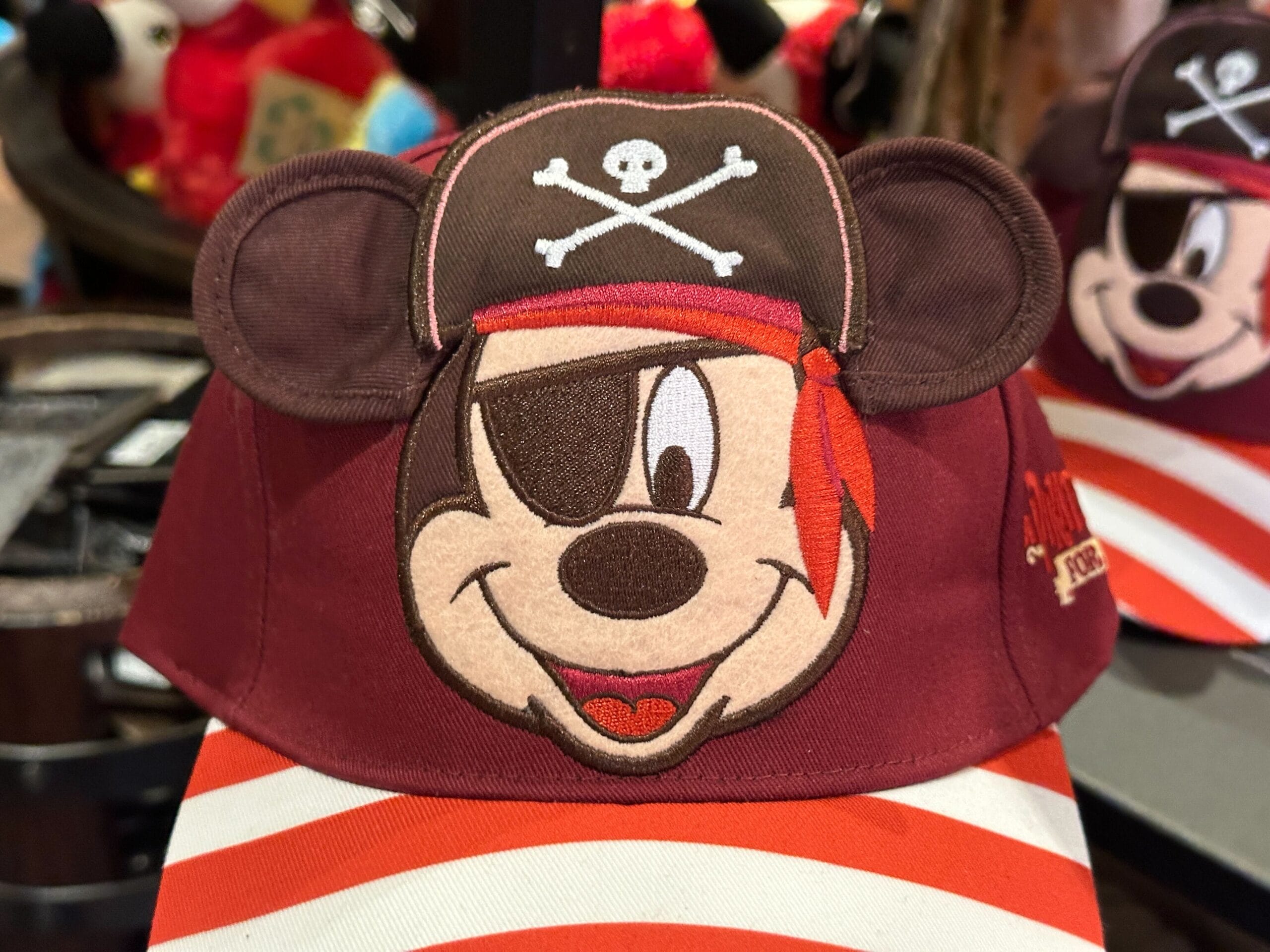 A Disney Parks hat with Mickey Mouse as a pirate, sporting an eyepatch, red bandana, and skull-and-crossbones pirate hat.
