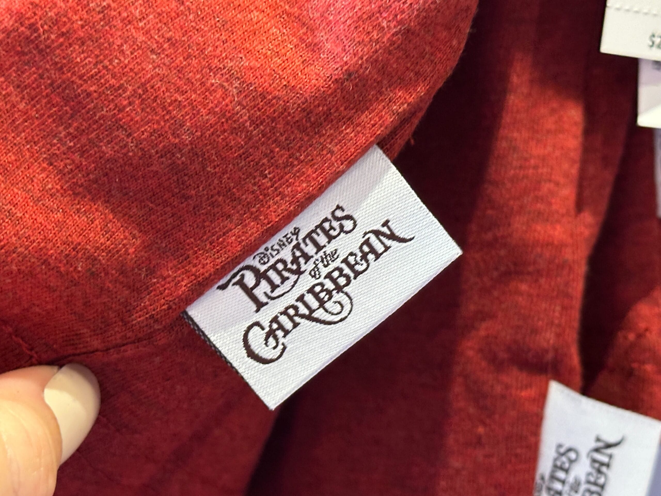 A white "Pirates of the Caribbean" tag, like those sold in Disney Parks, is attached to red fabric, with no castle visible.