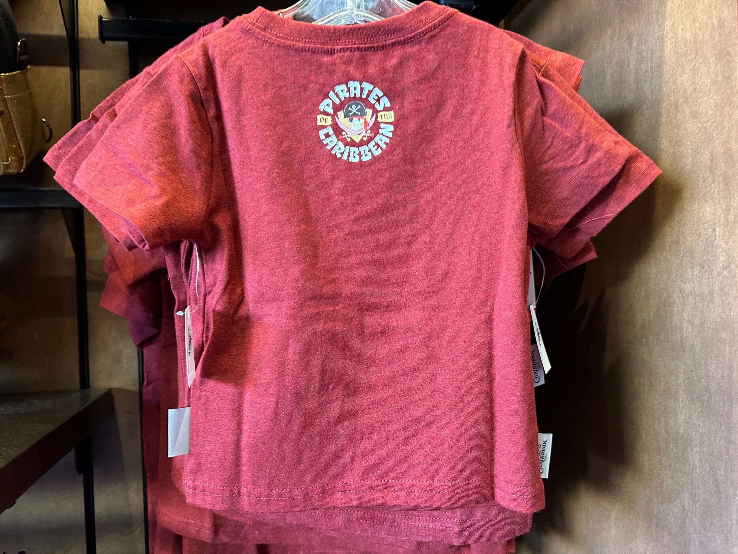 Red toddler t-shirt featuring a "Pirates of the Caribbean" logo and skull graphic, reminiscent of Disney Parks attraction designs.