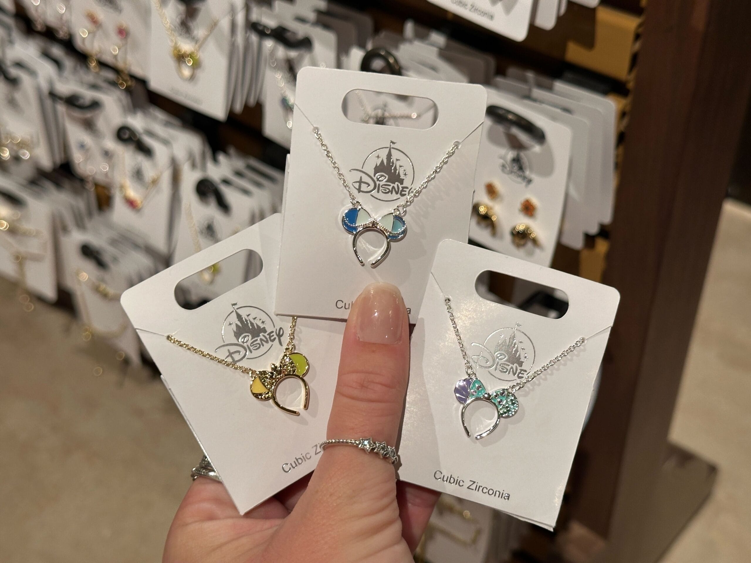 A hand displays three Disney cubic zirconia Mickey Mouse necklaces on cards, reminiscent of popular park merchandise.