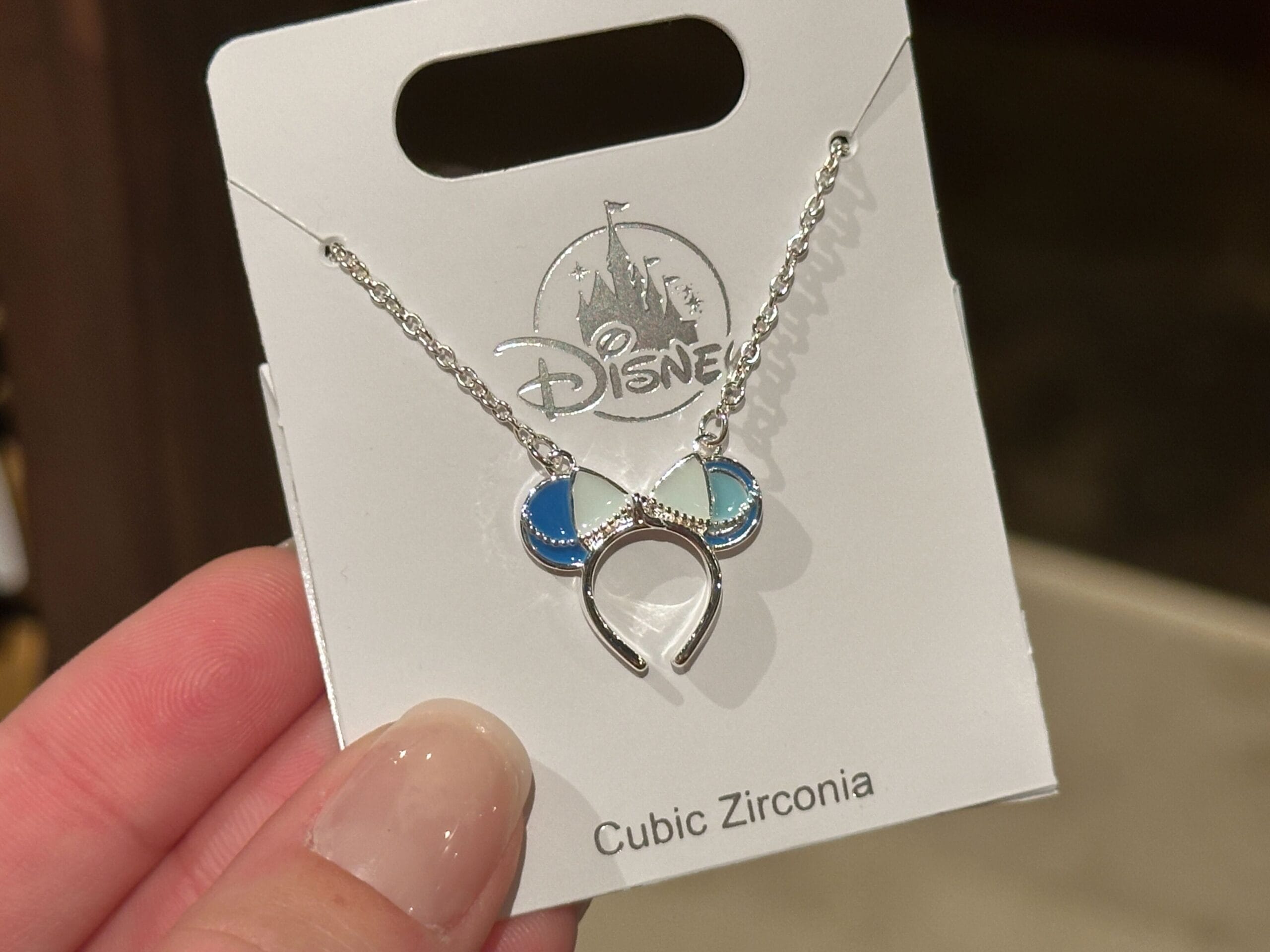 A silver necklace with a blue and white Minnie Mouse ear pendant sits on a Disney Parks card labeled "Cubic Zirconia.