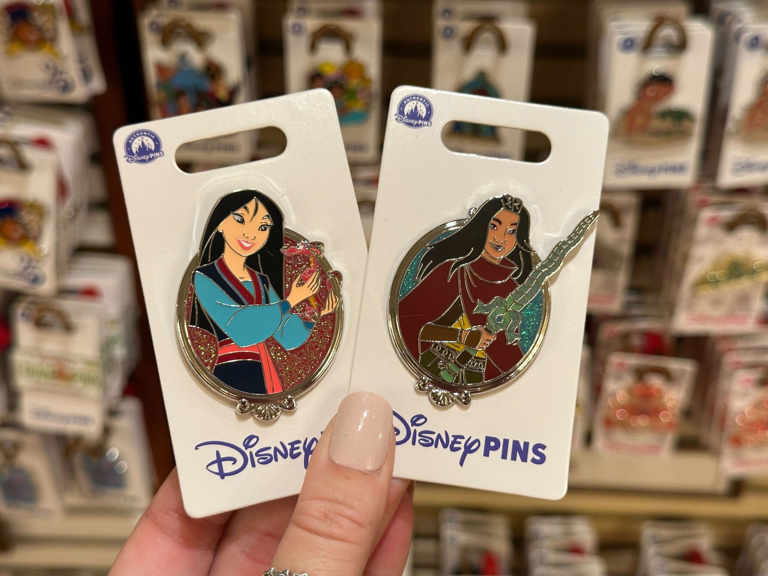 A hand shows two Disney Princess Sidekicks Pins on cards, with more pins and the iconic Walt Disney World setting softly blurred behind.