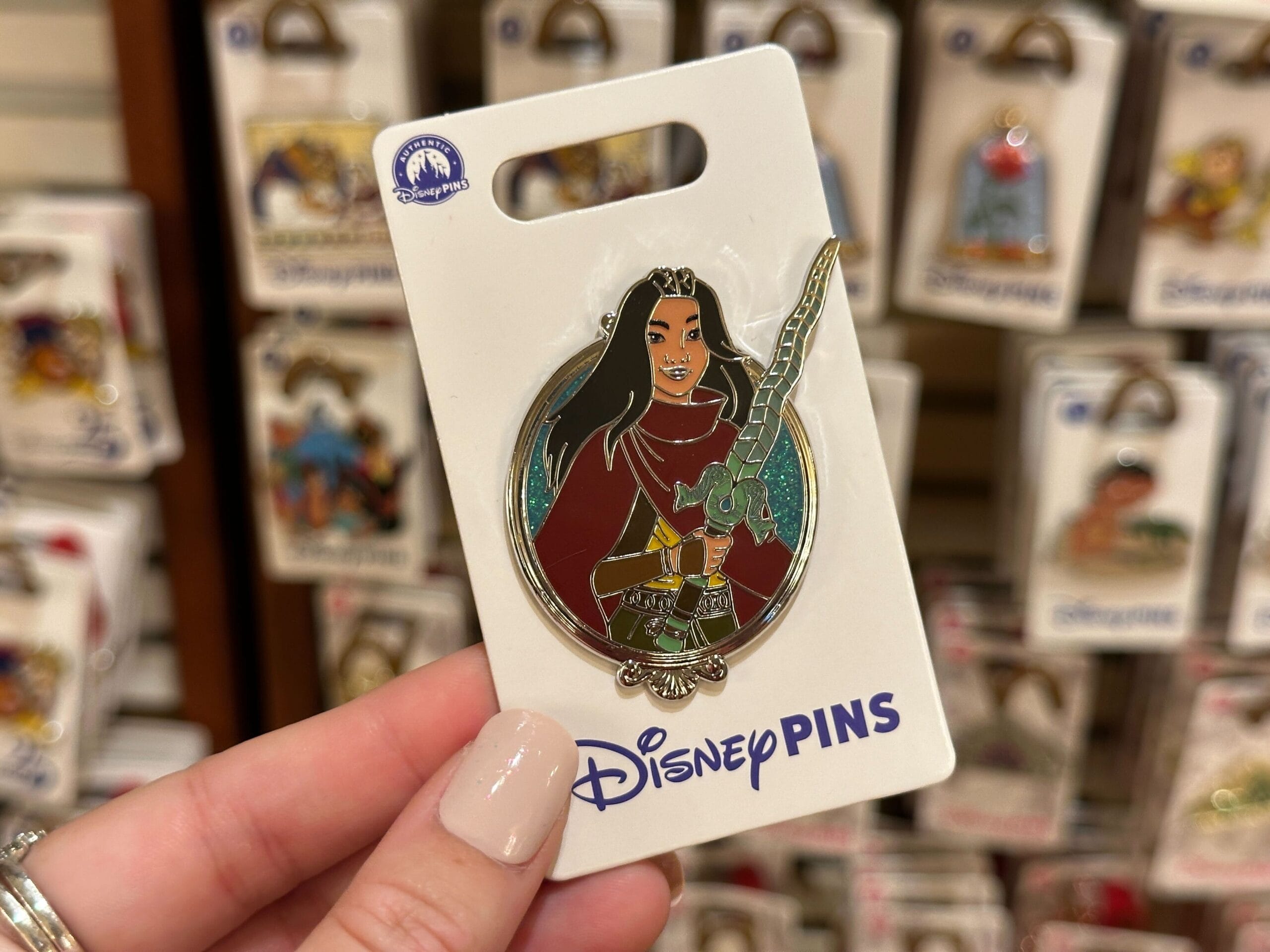 A hand holds a Disney Princess pin of Mulan with a sword on a Walt Disney World backing card, known for Cinderella Castle nearby.