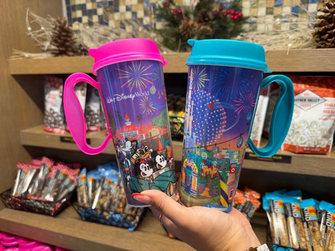 Two colorful Disney Resort Refillable Mugs featuring Mickey and Minnie are held in front of a store display with snacks.