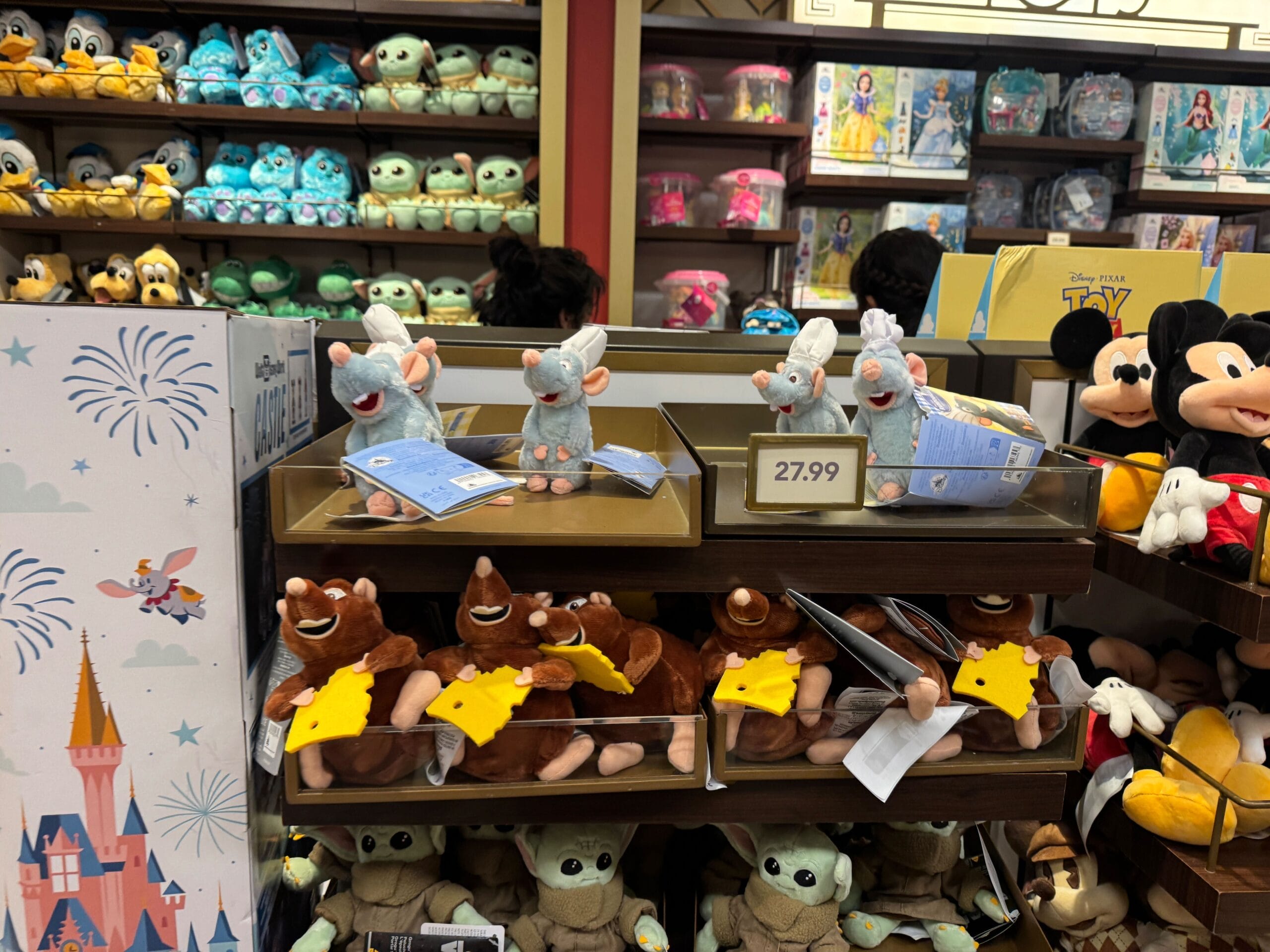 Plush Remy and Emile from Ratatouille displayed with other Disney plush at Walt Disney World, no castle like the iconic Cinderella Castle.