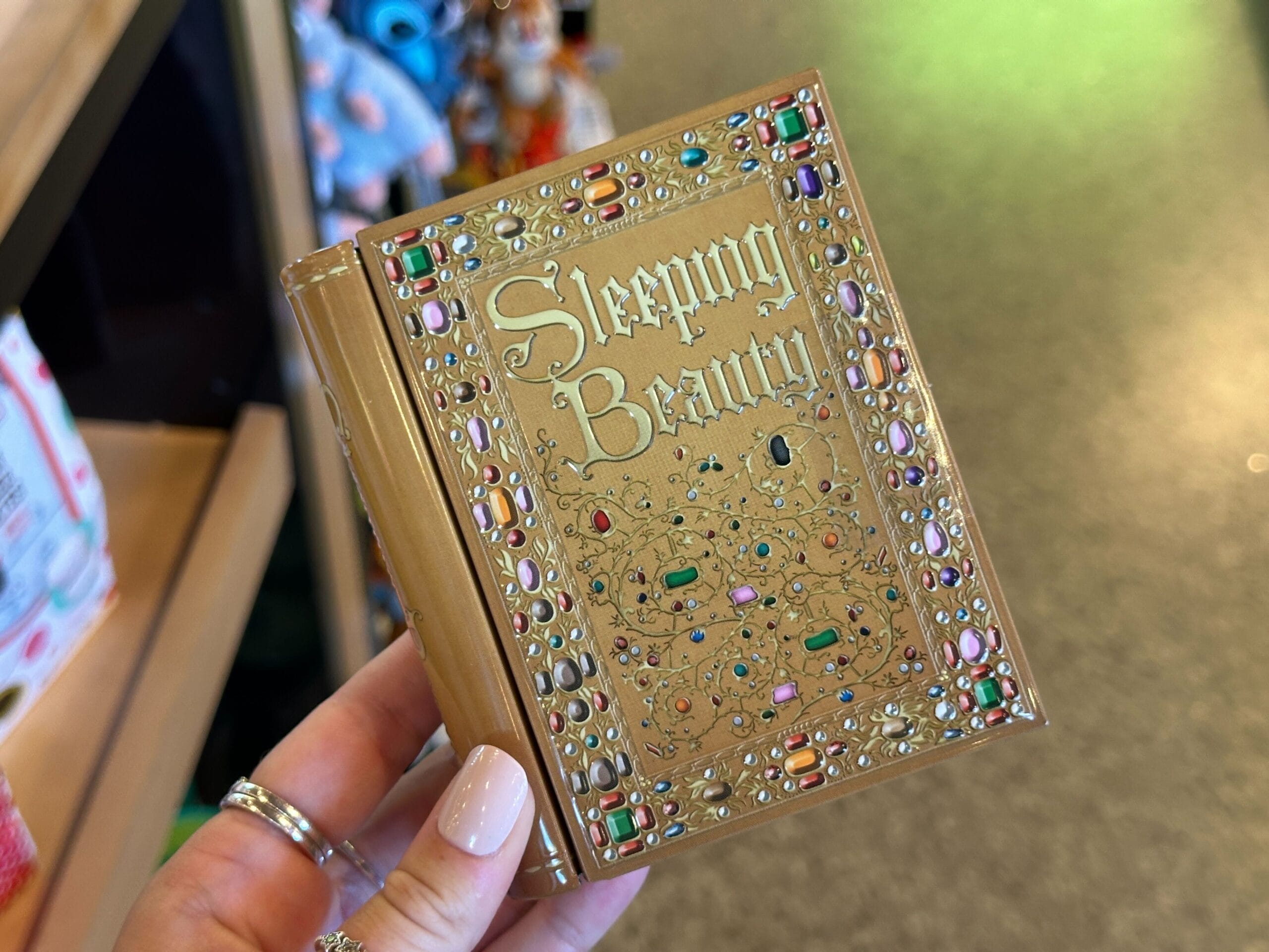 A hand holds a jeweled "Sleeping Beauty" book, its gold cover and gems reminiscent of Sleeping Beauty Castle at Disneyland.